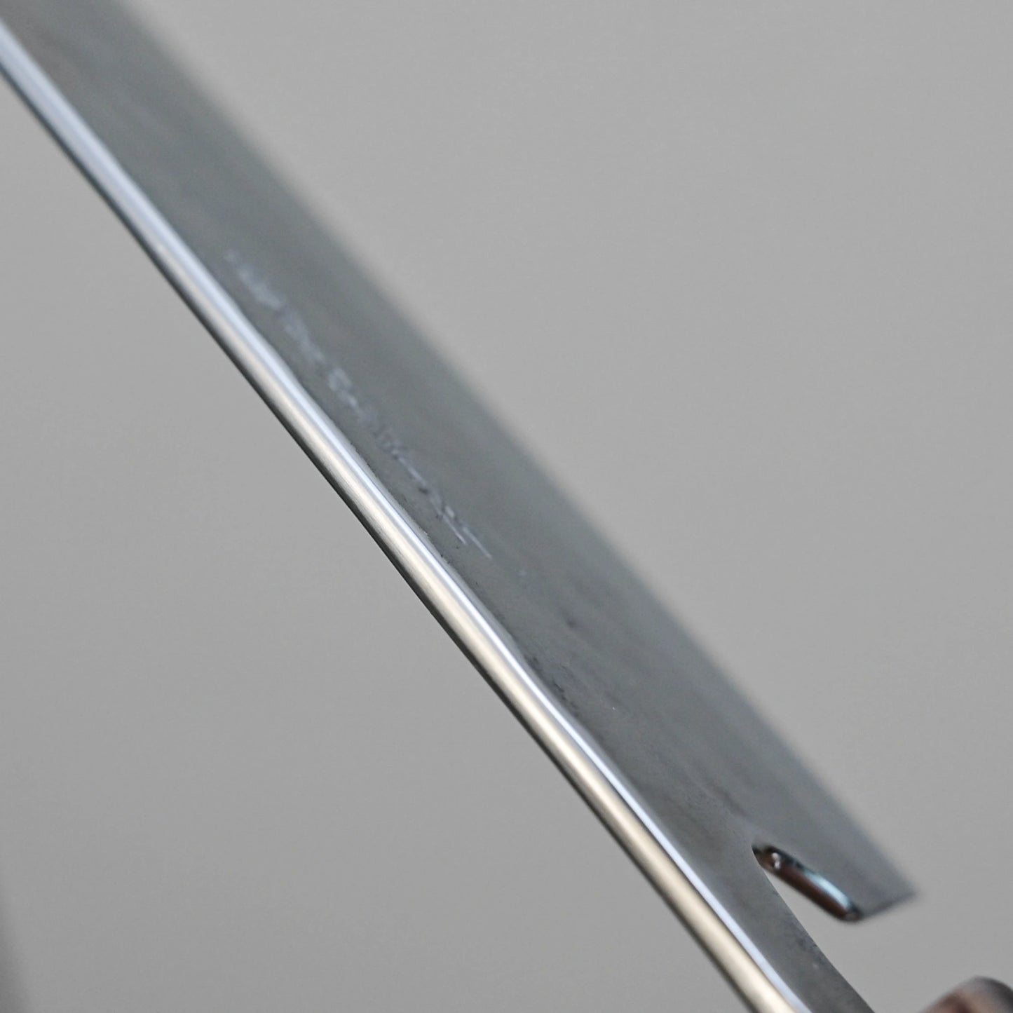 Close-up of the Teruyasu Fujiwara Maboroshi shirogami#1 wa-gyuto 210mm, featuring a custom handle, saya, and polished choil, highlighting its straight edge and notch against a plain gray background.