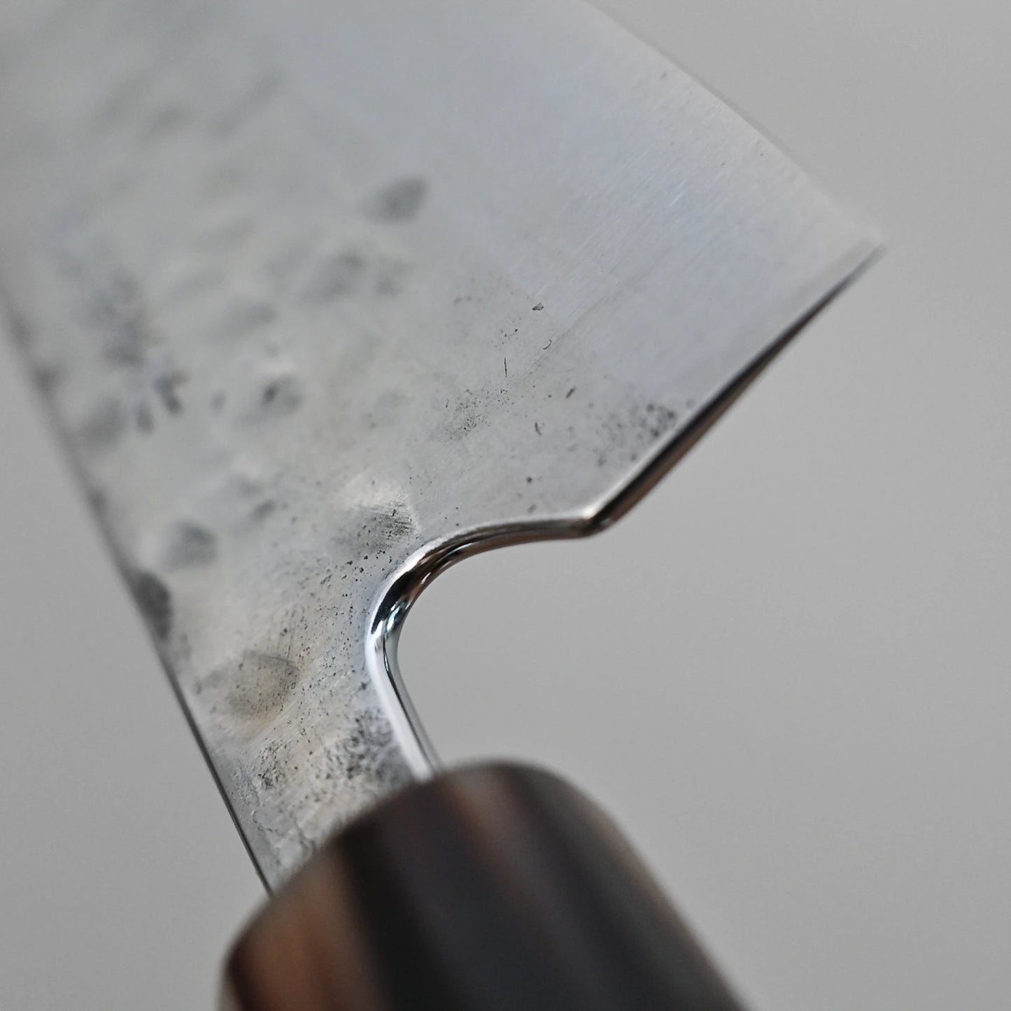 Close-up of the Teruyasu Fujiwara Maboroshi Shirogami #1 Wa-Gyuto 210mm, featuring a hammered blade, sharp polished choil, and a custom handle with saya. The focused detail highlights the knifes superb craftsmanship.