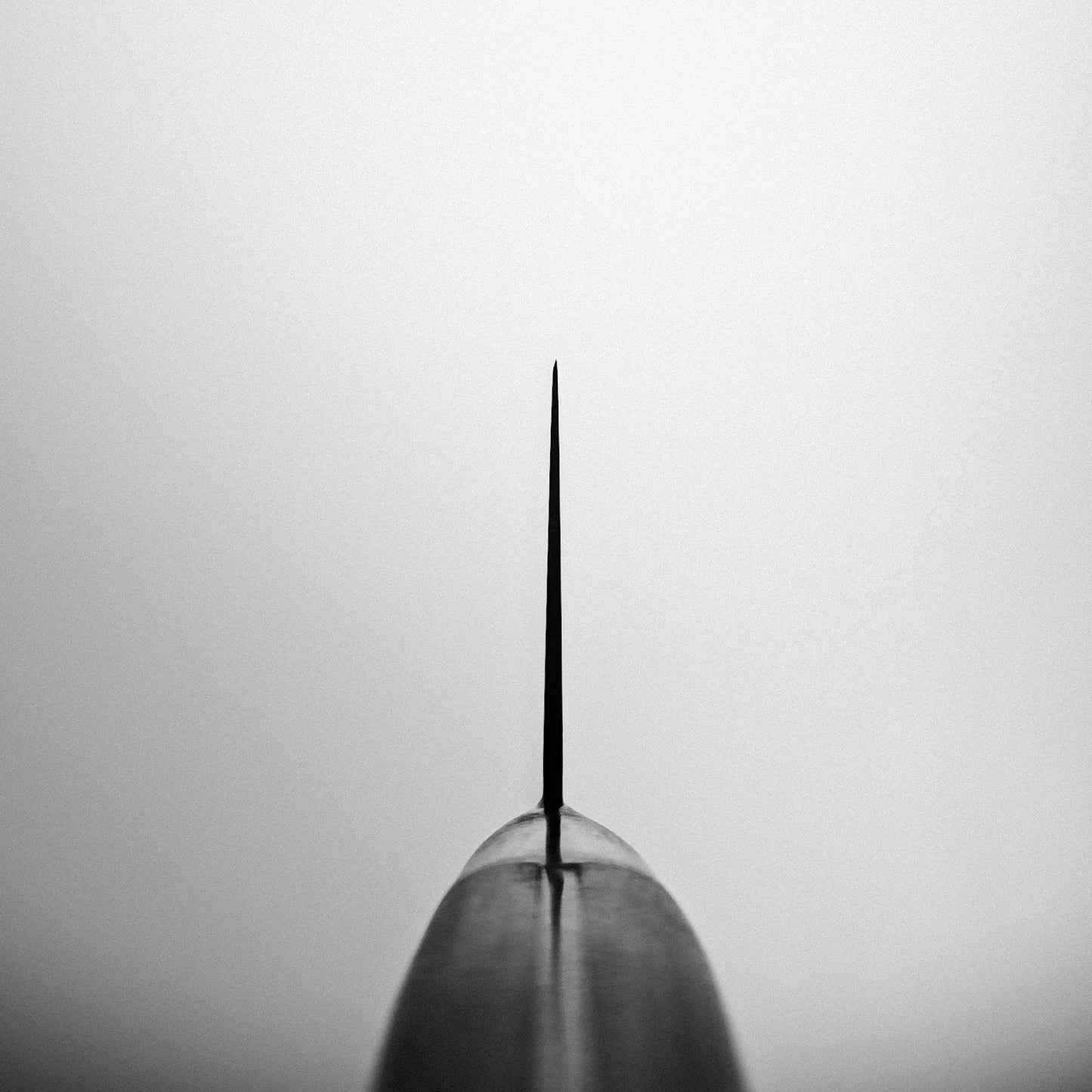 A black and white close-up highlights the sharp, symmetrical tip of the Misono Molybdenum gyuto 210mm chef’s knife, centered against a plain light background.