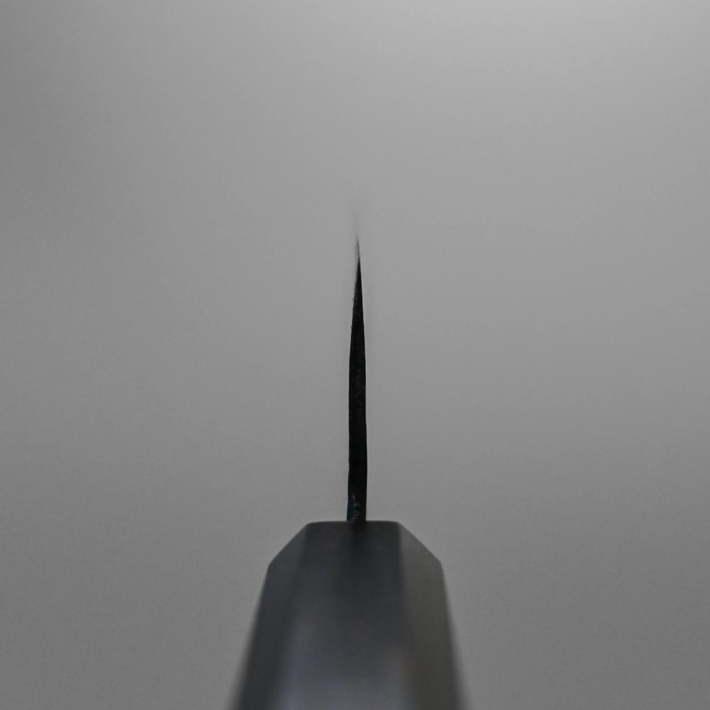 Choil shot of the Hatsukokoro kurouchi aogami#2 bunka 165mm knifes blade edge, crafted with Aogami #2 steel and a kurouchi finish, photographed from the tip against a blurred, neutral background.
