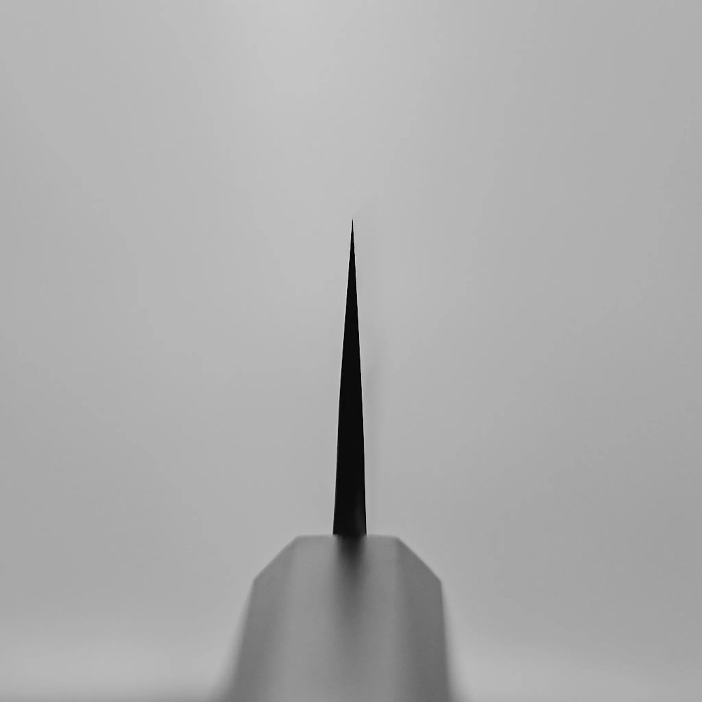 A close-up, centered view of the Hatsukokoro x Yoshikane kurouchi nashiji shirogami#2 gyuto 210mm blade’s sharp edge, photographed from the tip down the spine against a plain light gray background.