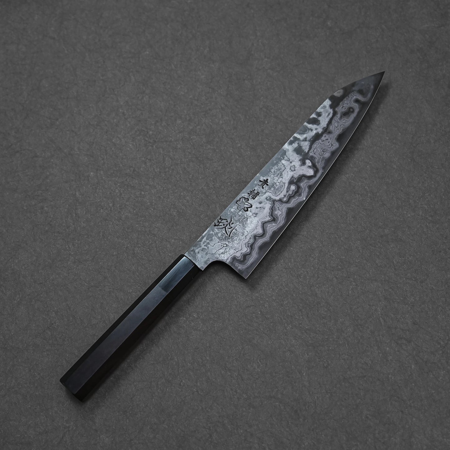 Japanese damascus chef’s knife with dark wooden handle, etched kanji characters, and layered steel pattern.