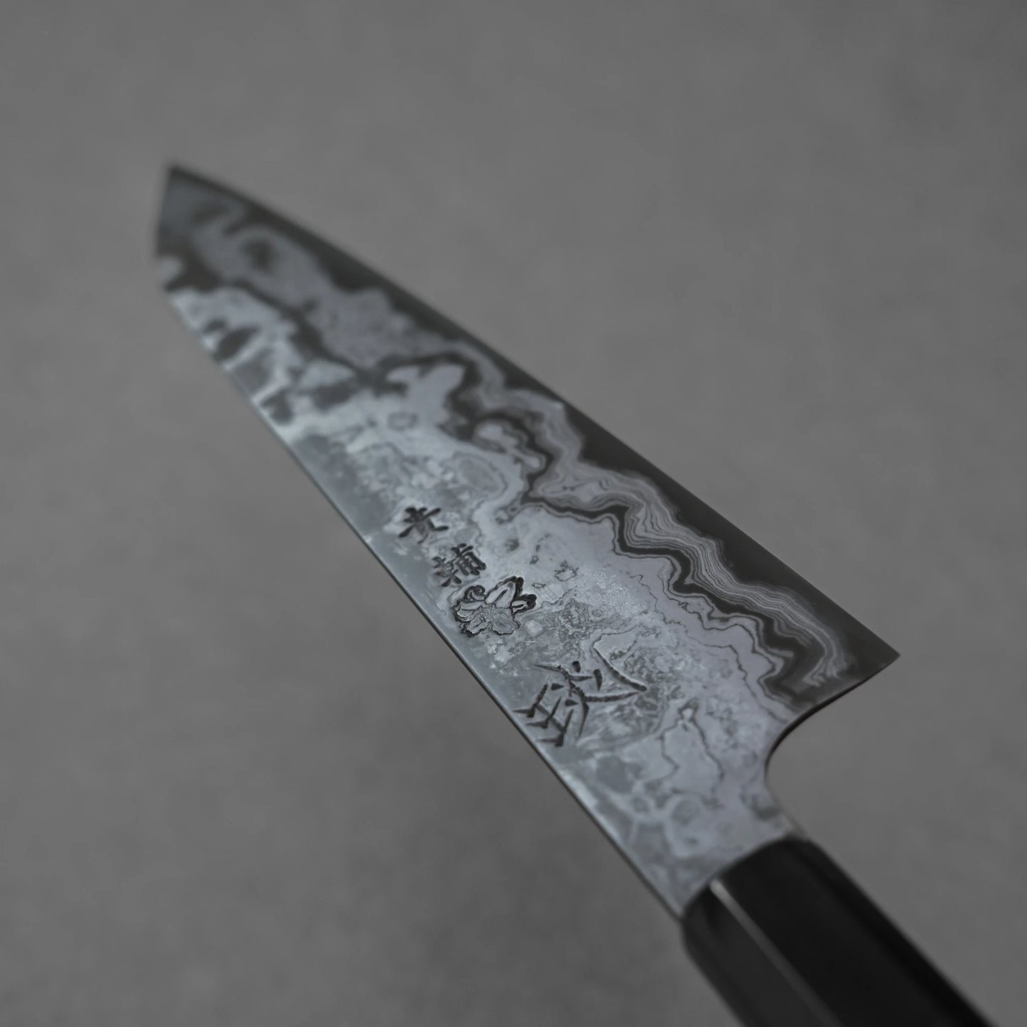 Damascus steel knife blade with bold forged wave patterns and deeply engraved Japanese kanji characters in center focus.