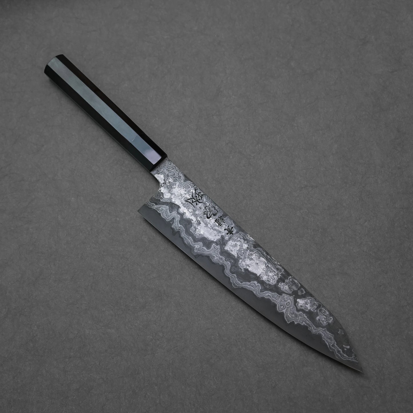 Etched damascus gyuto knife with a textured blade on a gray background