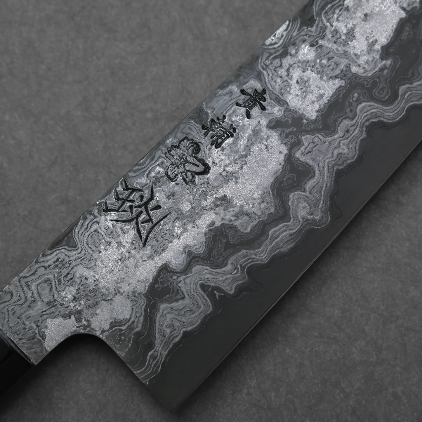 Close-up of a Damascus steel knife blade with engraved characters on a dark background
