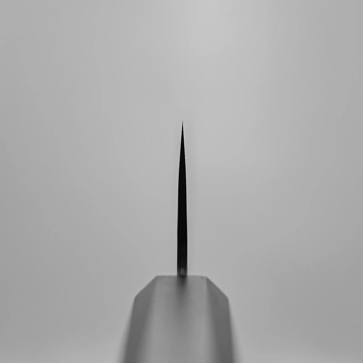 A close-up, front-facing view of the tip of the Nigara tsuchime damascus VG10 bunka 180mm knife against a plain light gray background, with the centered blade showcasing its sharp point and refined craftsmanship.