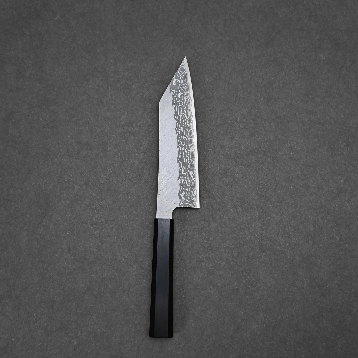 The Nigara tsuchime damascus VG10 bunka 180mm knife with a black handle rests on a flat, dark gray surface.