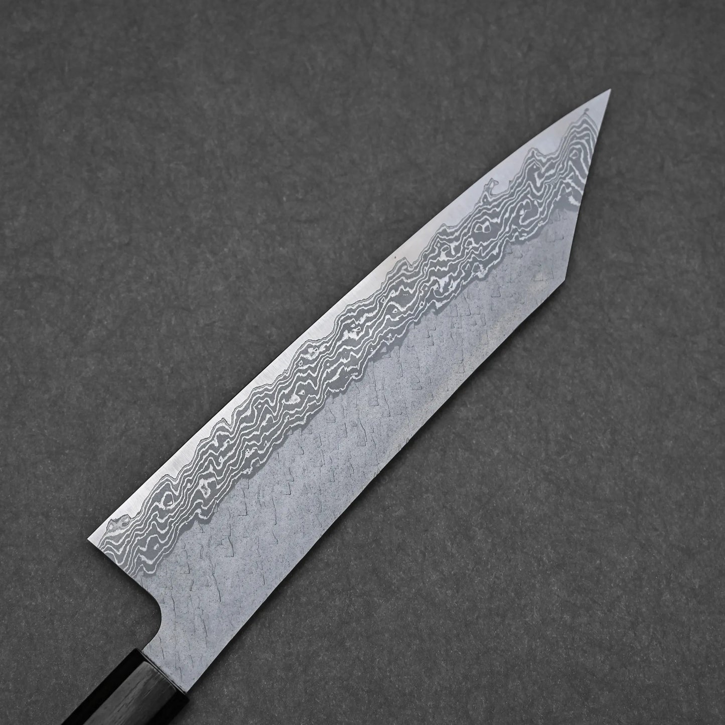 A close-up of the Nigara tsuchime damascus VG10 kiritsuke gyuto 210mm shows its wavy-layered blade, pointed tip, and hammered finish, expertly crafted from premium Takefu VG10 steel on a dark surface.