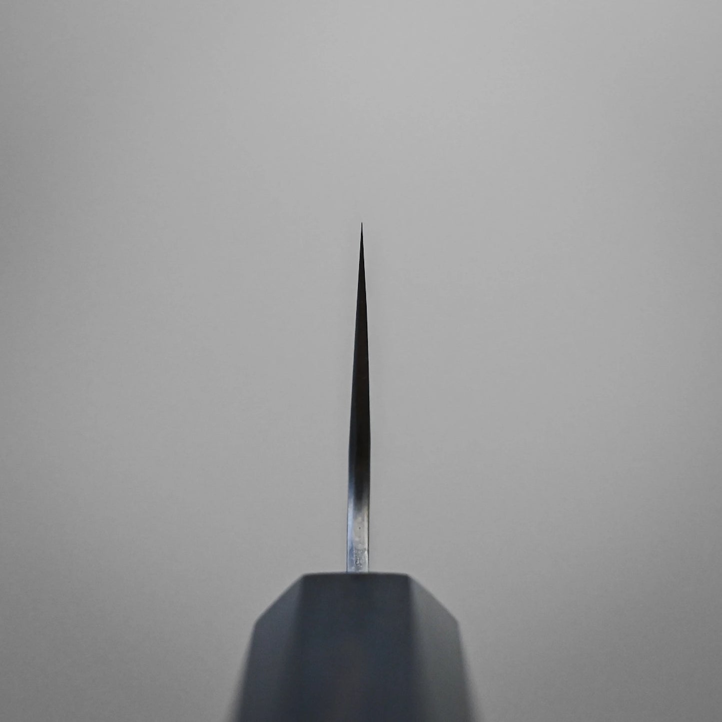 Choil shot of Nigara Hamono Nigara tsuchime damascus VG10 gyuto 210mm knife blade against a plain gray background.