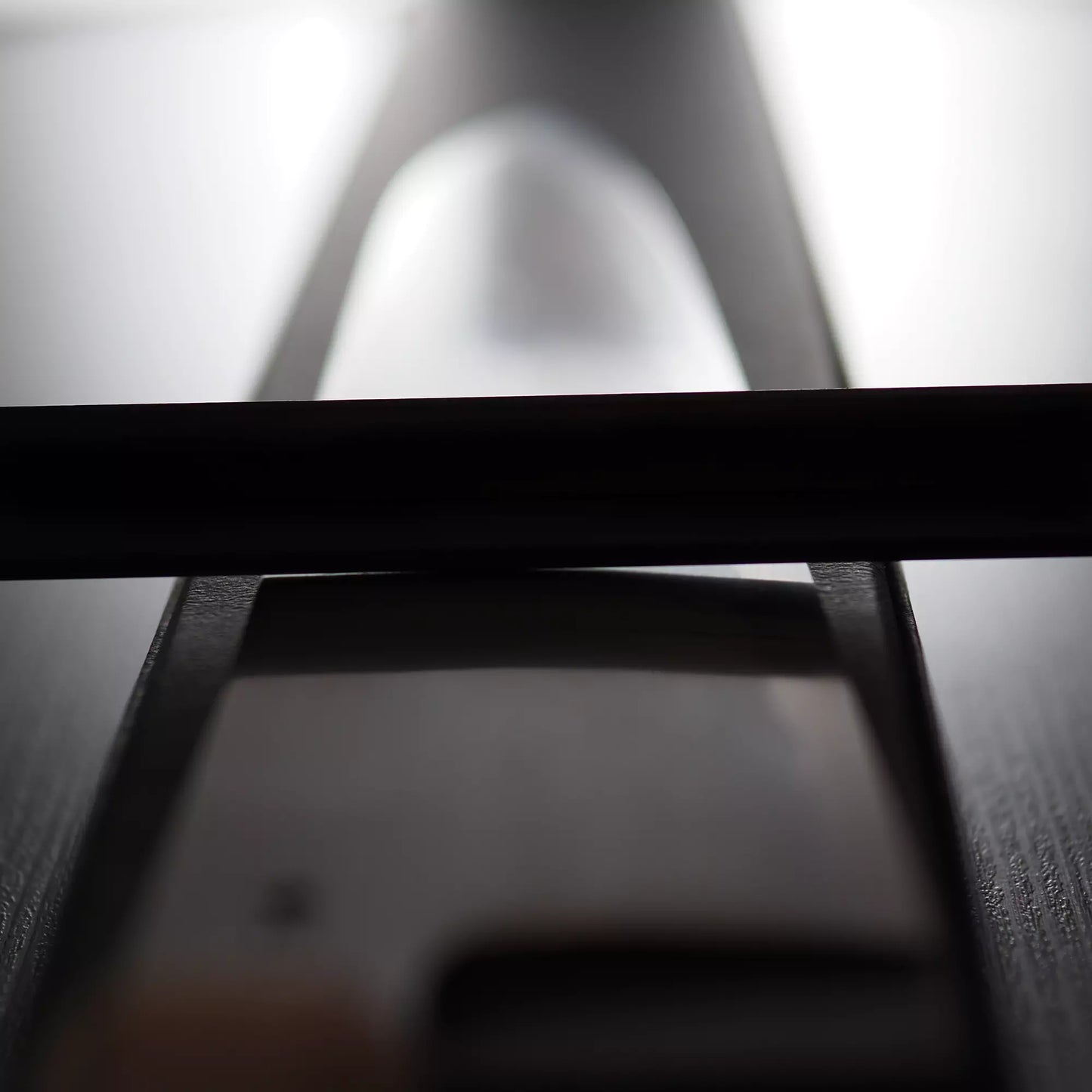 A close-up, out-of-focus photo of a Satoshi Nakagawa Nakagawa bokashi shirogami#1 tall gyuto 240mm lying flat on a dark surface, light reflecting off the blade. The handle is in the foreground; the blade extends into the background.