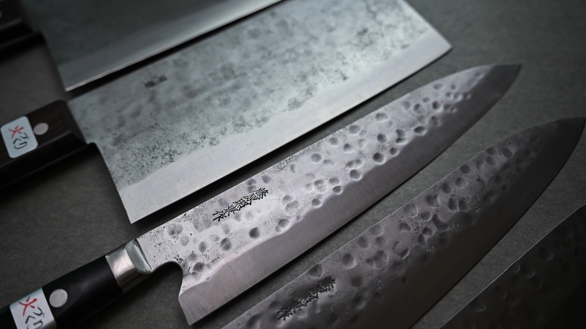 Set of Japanese chef knives and chuka bocho with hammered finish on a dark background