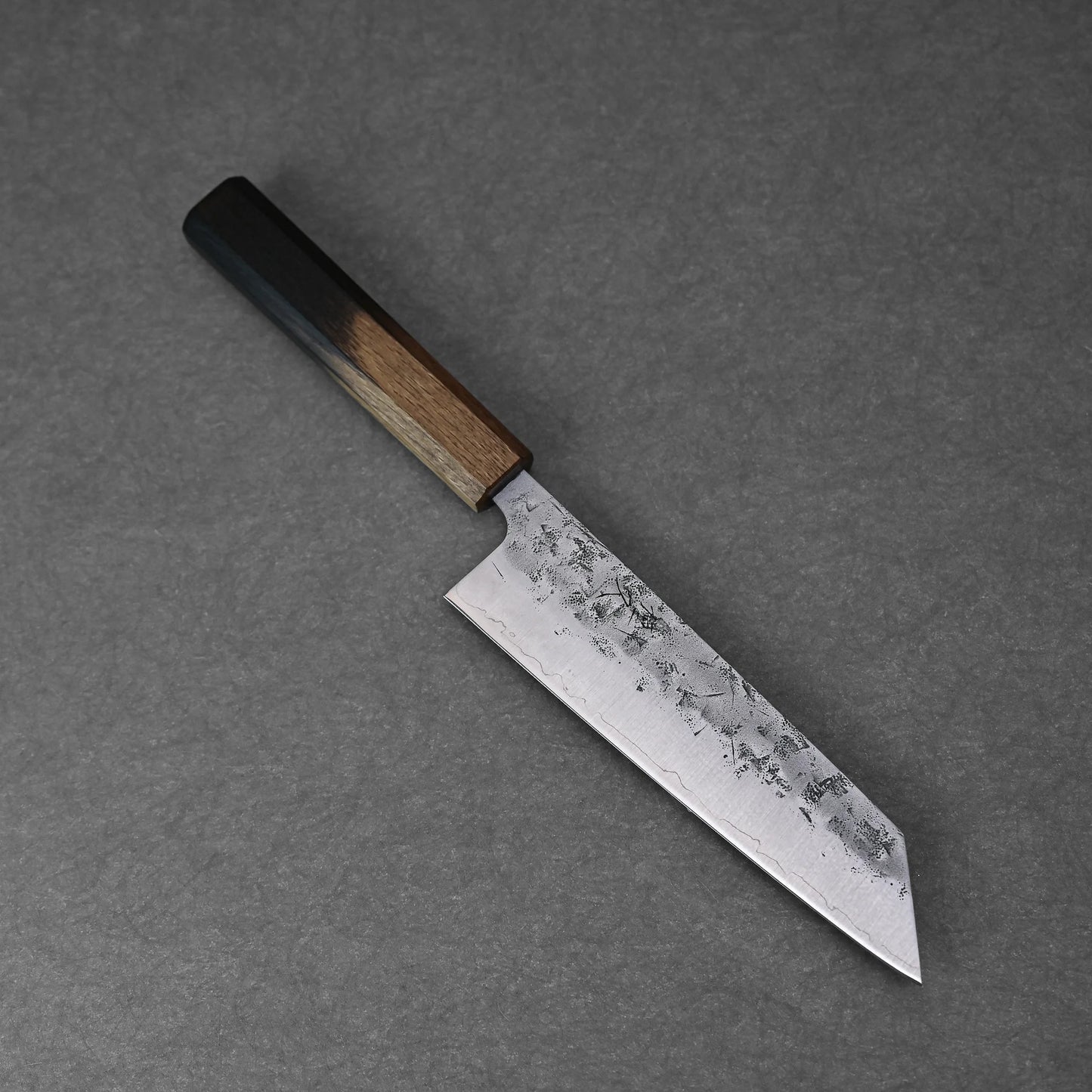 The Tsunehisa nashiji SLD bunka 170mm, showcasing Japanese craftsmanship with a dark wooden handle and textured rectangular SLD steel blade, rests elegantly on a gray surface.