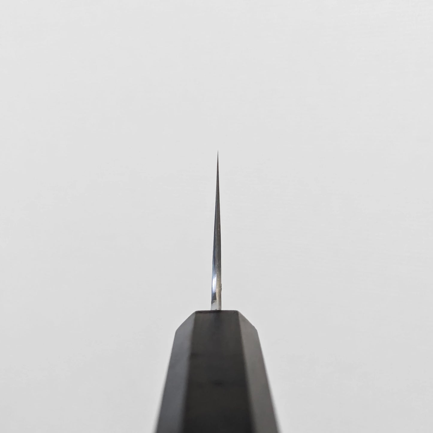 Japanese knife featuring a visible choil shot with a polished finish and damascus steel wave patterns extending into the choil area; photographed to highlight the edge transition and blade precision near the handle.
