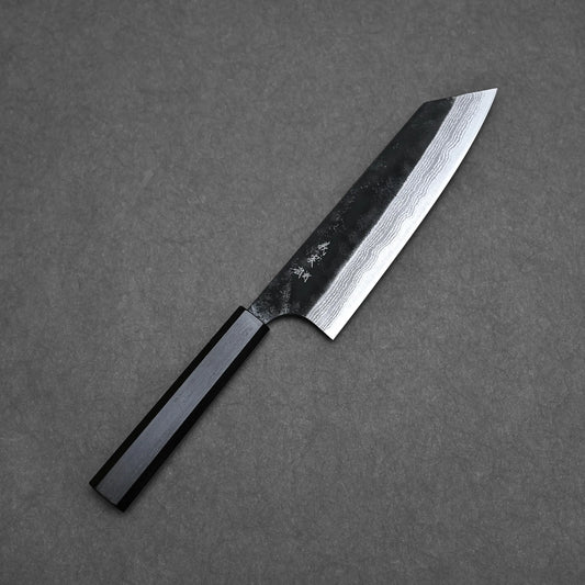 A Yoshimi Kato Aogami Super bunka knife from Echizen, Japan, with a dark wooden handle and a Damascus-patterned steel blade, lies on a gray textured surface.