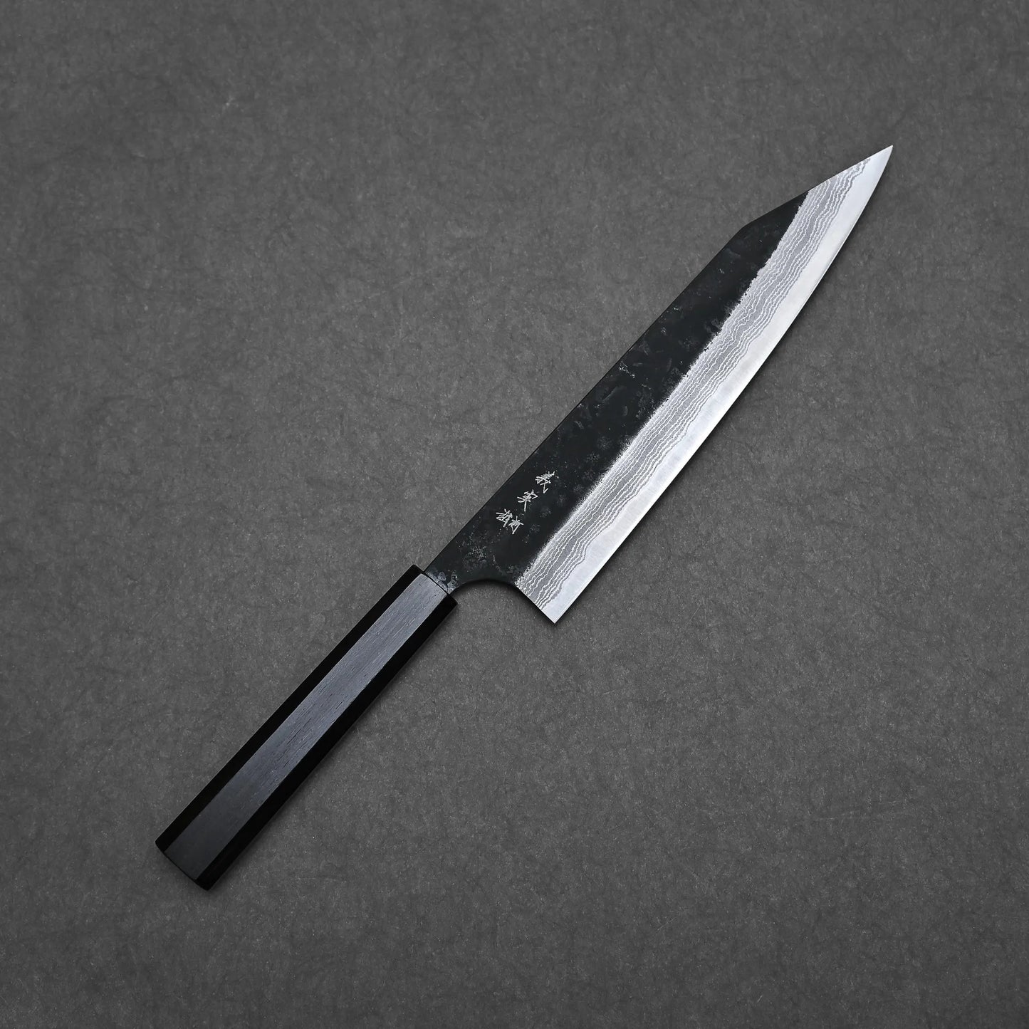The Yoshimi Kato kurouchi damascus AS kiritsuke gyuto 210mm, a Japanese kitchen knife with a dark handle, sharp textured blade, visible patterns, and Japanese characters near the handle, is crafted from premium Aogami Super steel.
