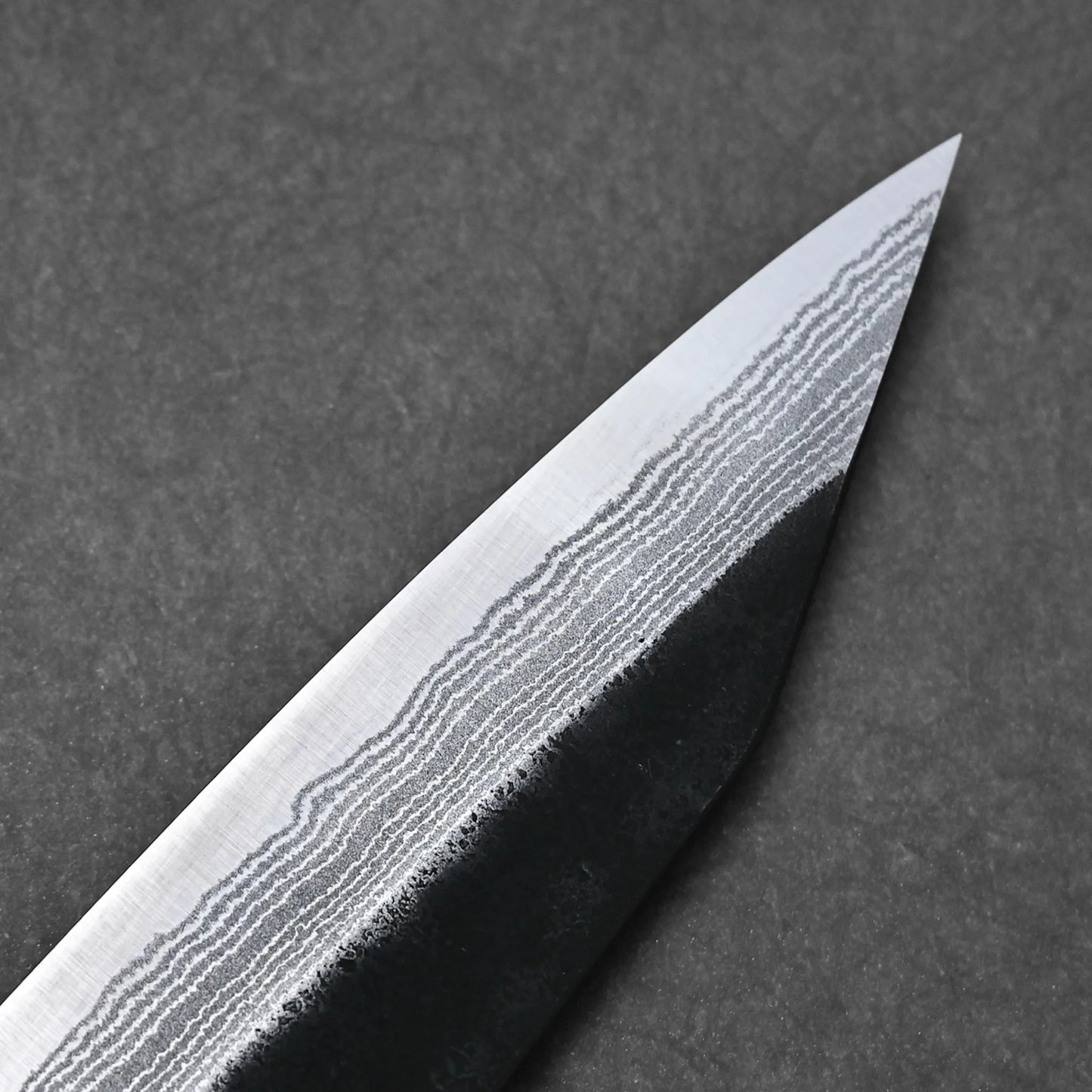 Close-up of the Yoshimi Kato kurouchi damascus AS kiritsuke gyuto 210mm, featuring Aogami Super steel with striking Damascus layered patterns on the blade, set against a dark background.