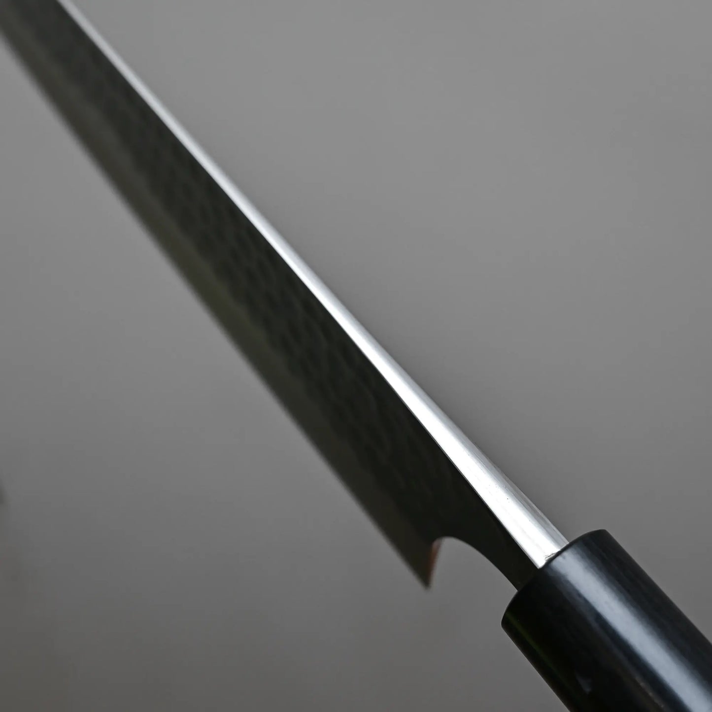 Close-up of the spine and handle of the Anryu tsuchime aogami#2 gyuto 210mm by Anryu, showing its hammered Aogami #2 carbon steel blade against a plain gray background.