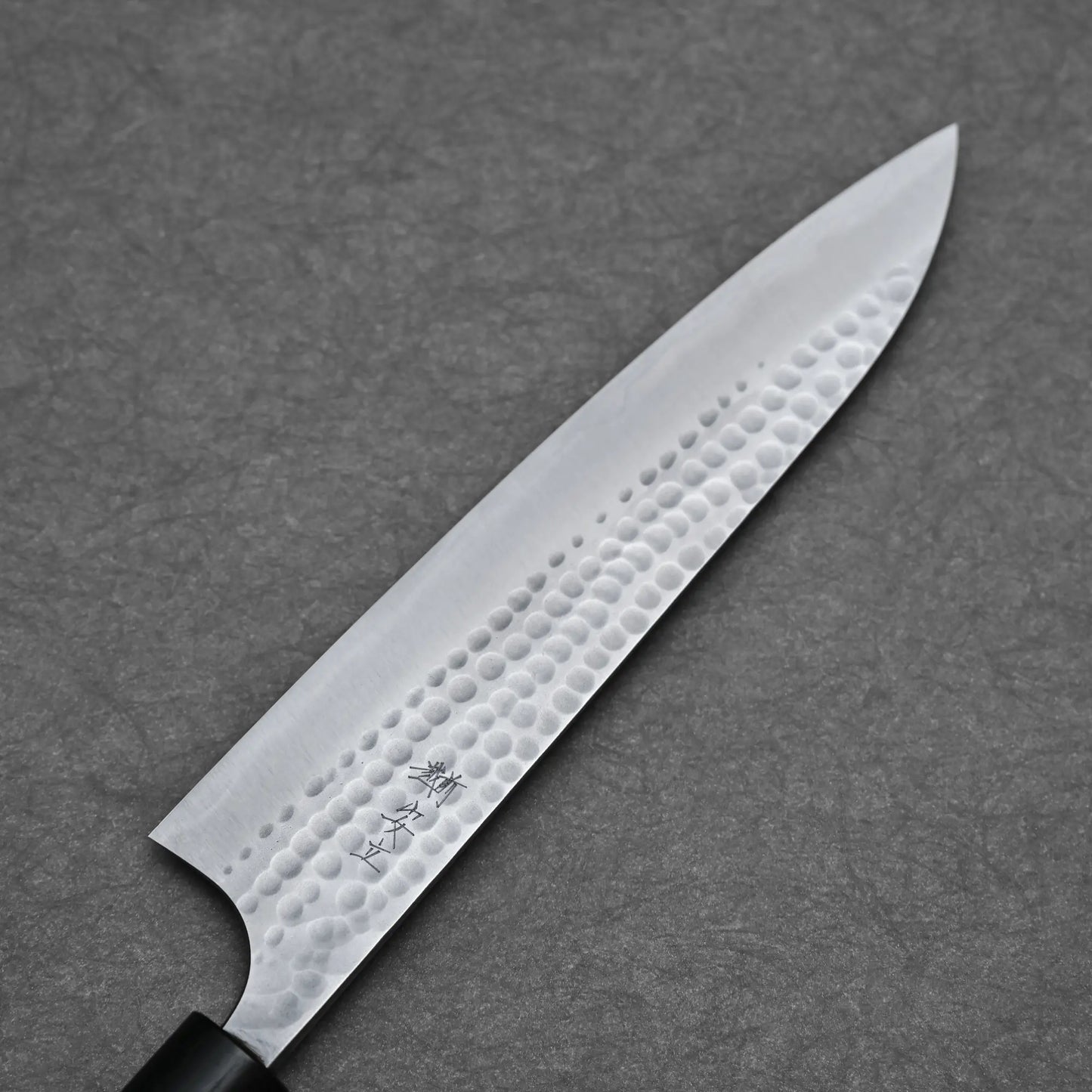 A close-up of the Anryu tsuchime aogami#2 gyuto 210mm by Anryu, showcasing its hammered Aogami #2 carbon steel blade with engraved kanji, set against a dark gray textured background.