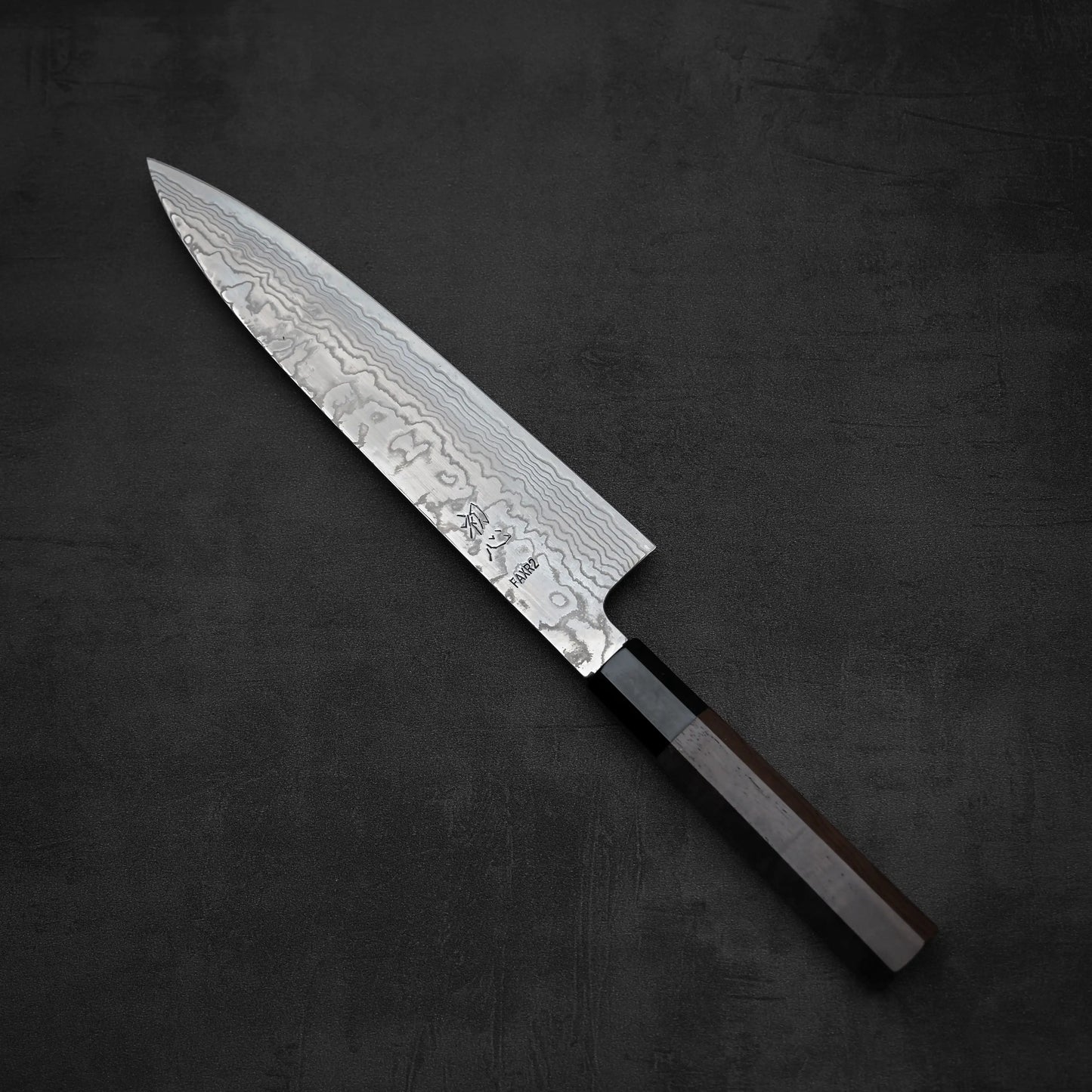 The Hatsukokoro FAXR2 damascus gyuto 240mm, a Japanese-style chefs knife with a Damascus steel blade and dark wooden handle, by Hatsukokoro is displayed on a black textured background.