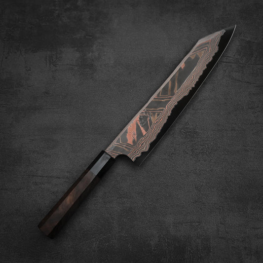 The Hatsukokoro x Nigara Irodori aogami#2 damascus kiritsuke gyuto 270mm features a dark wooden handle and polished, patterned blade, resting elegantly on a dark textured surface.