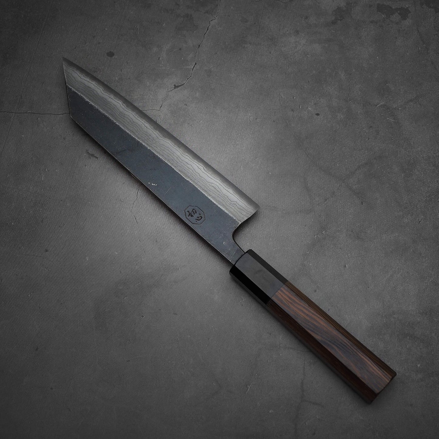 Top view of Hatsukokoro Kumokage kurouchi damascus aogami#2 bunka knife where tip is facing upper left