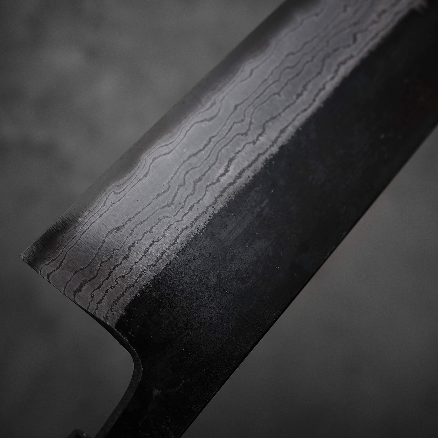 Close up view of Hatsukokoro Kumokage kurouchi damascus aogami#2 nakiri knife. Image focuses on the damascus patterns