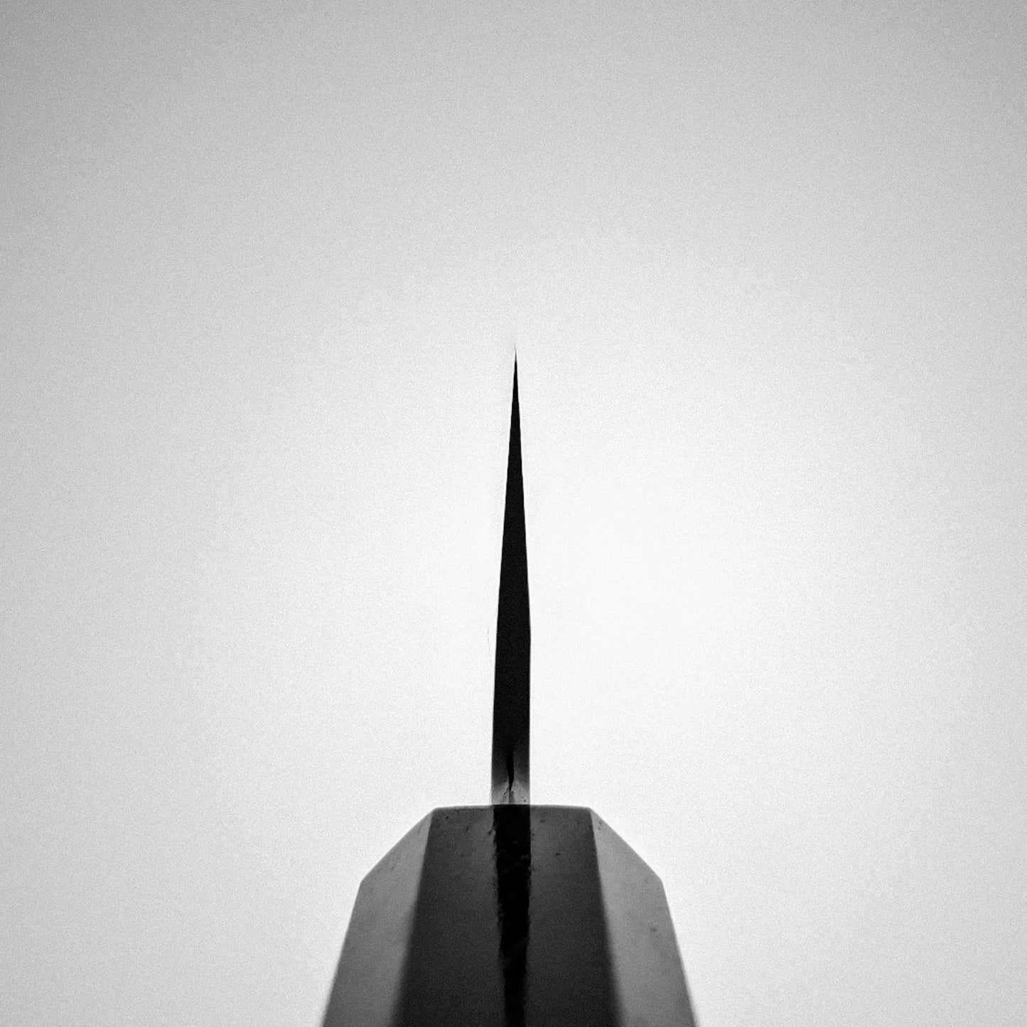 A close-up highlights the sharp tip of a Nakagawa aogami#1 damascus bunka 180mm by Satoshi Nakagawa, centered against a soft, blurred background in striking black and white—evoking its fine edge and minimalist design.