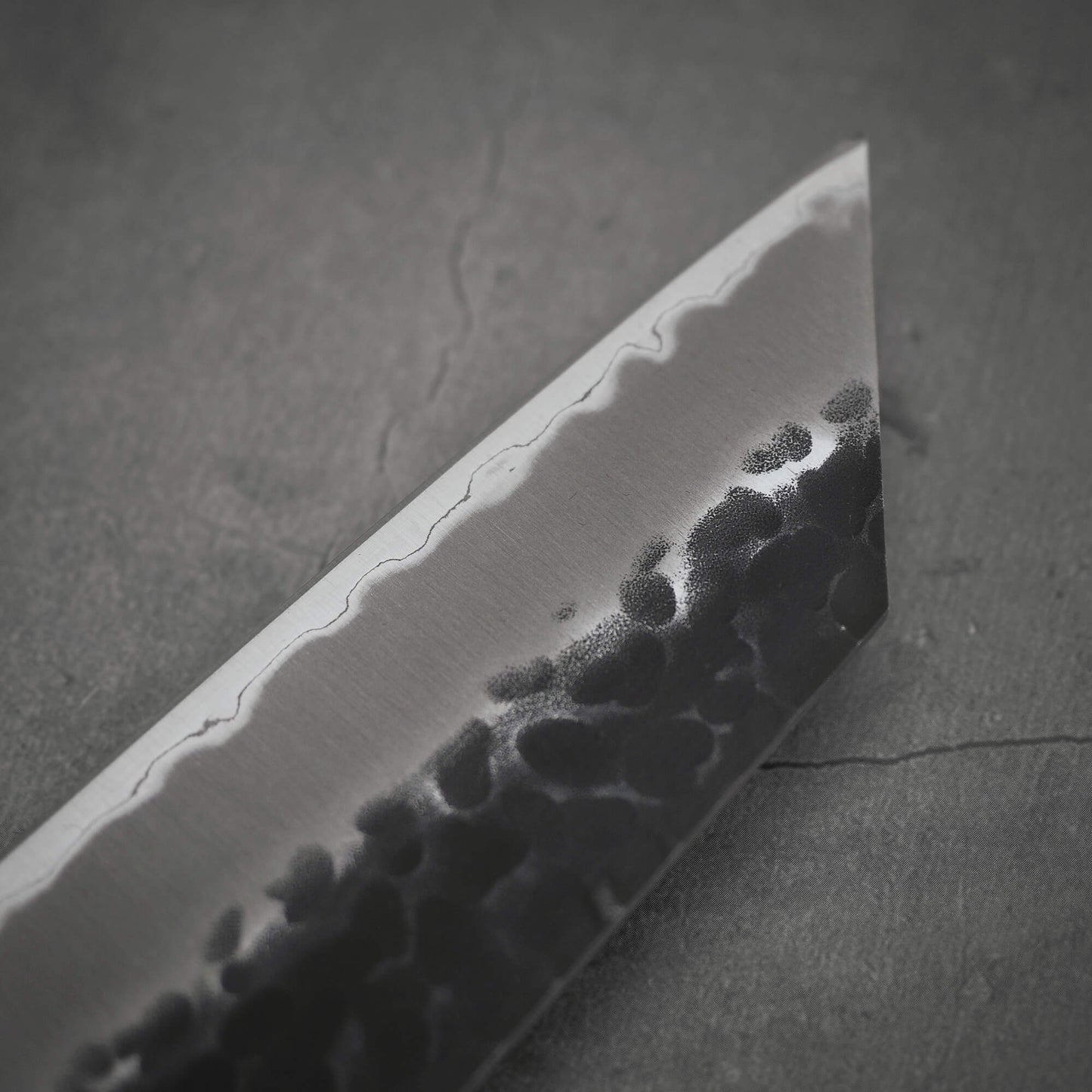 Close up view of Ittosai Kotetsu tsuchime kurouchi aogami super kiritsuke gyuto. Image focuses on the tip area of the back side