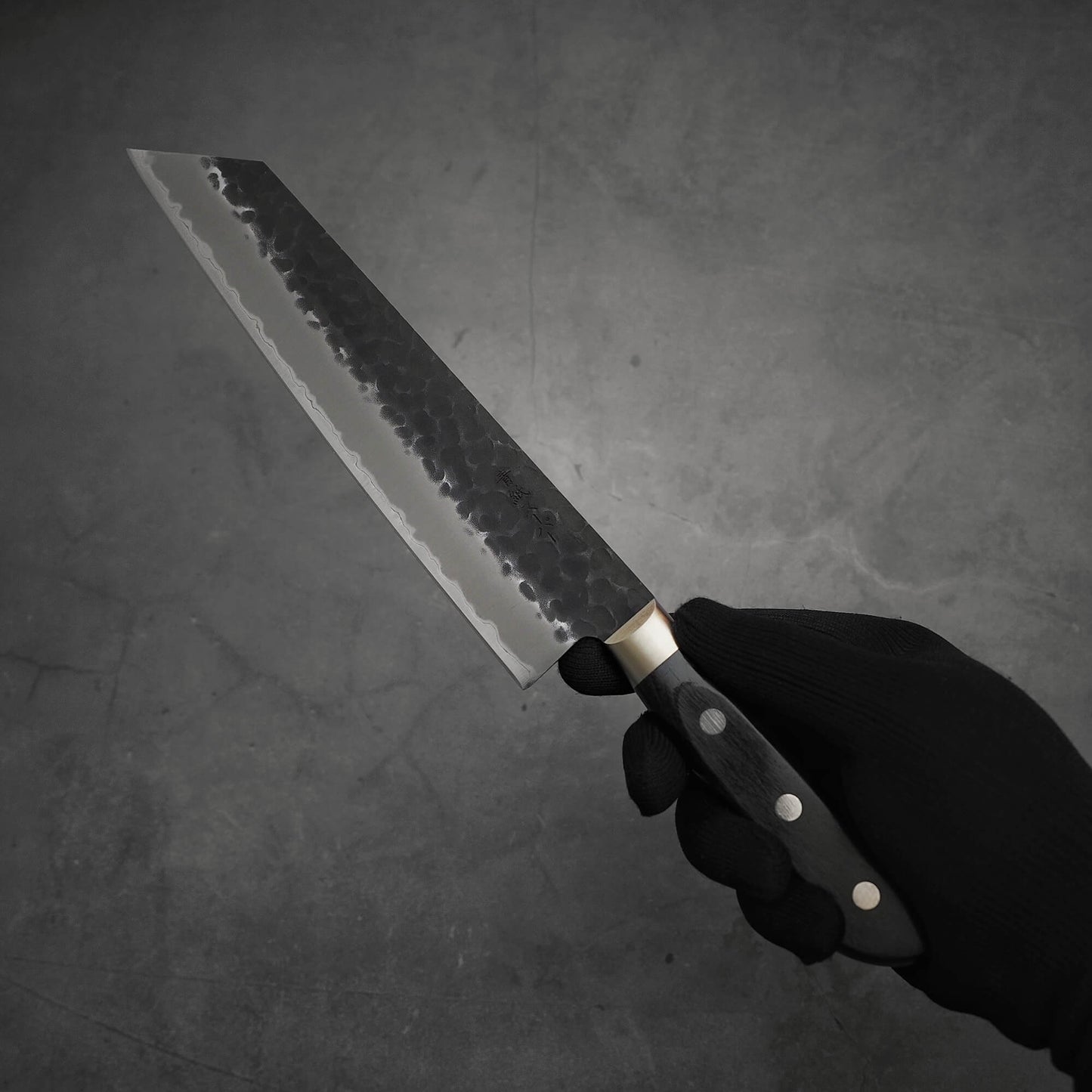 Hand holding Ittosai Kotetsu tsuchime kurouchi aogami super kiritsuke gyuto showing the left side of the knife