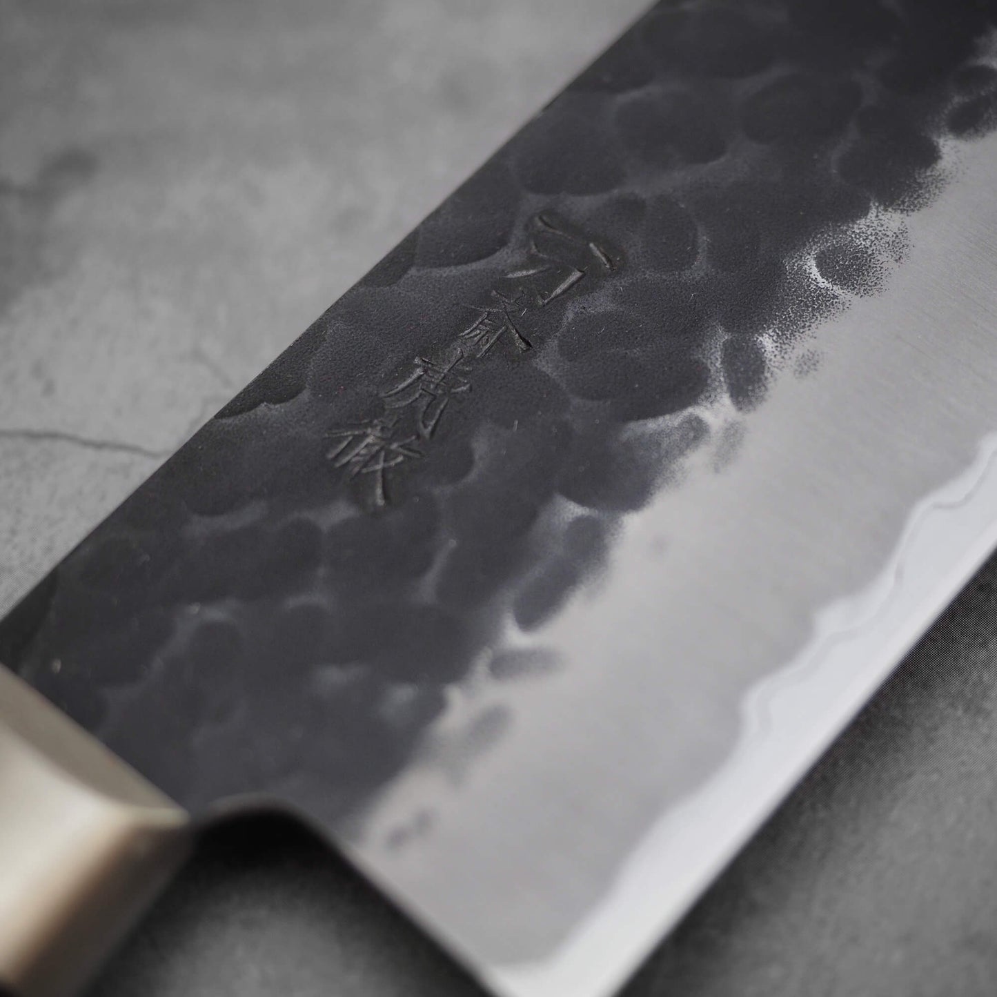 Close up view of Ittosai Kotetsu tsuchime kurouchi aogami super kiritsuke gyuto. Image focuses on the kanji side