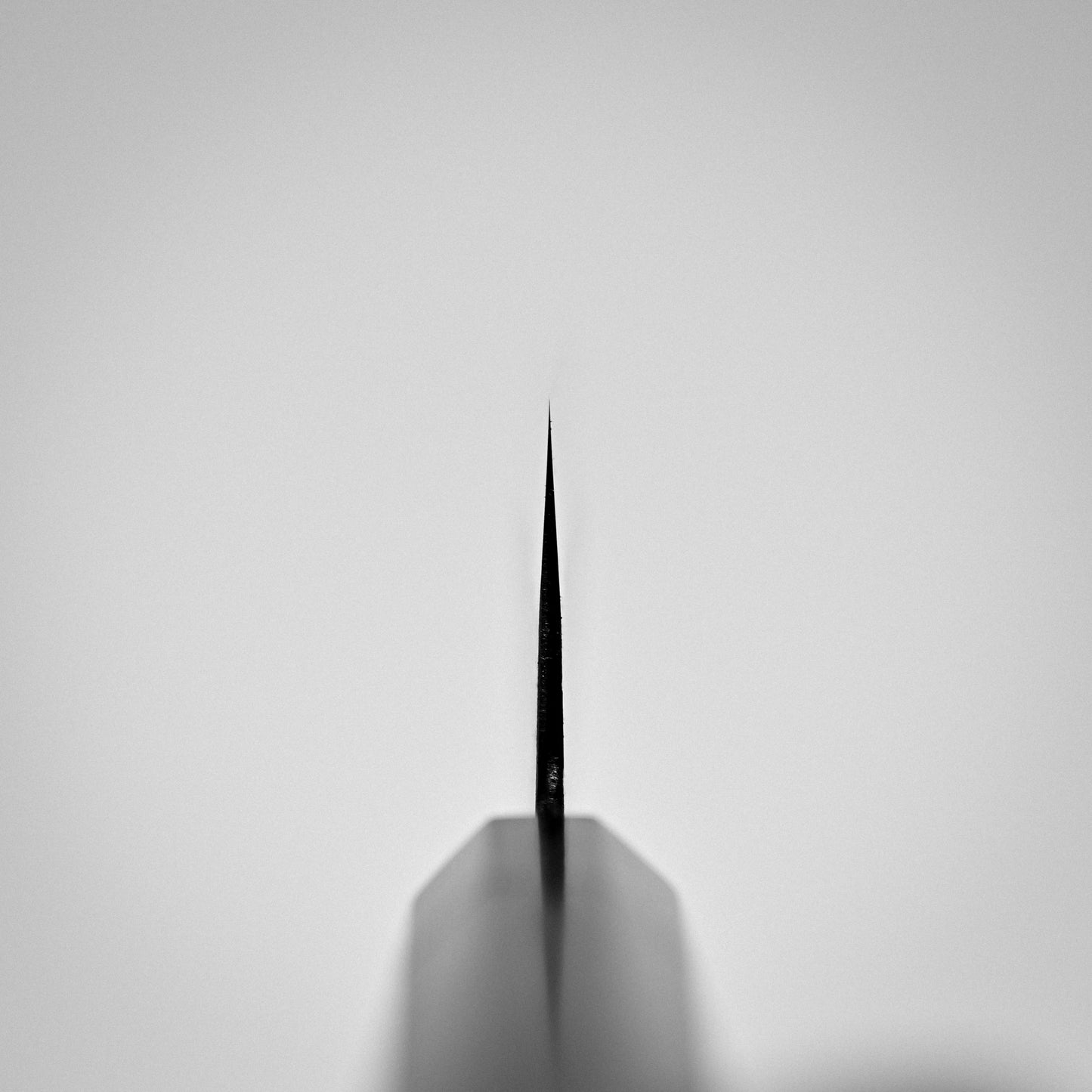 Close-up of the pointed tip of the Hinoura kurouchi nashiji AS (stainless clad) hakata 180mm knife by Hinoura, handmade from Aogami Super steel, photographed head-on against a plain light gray background.
