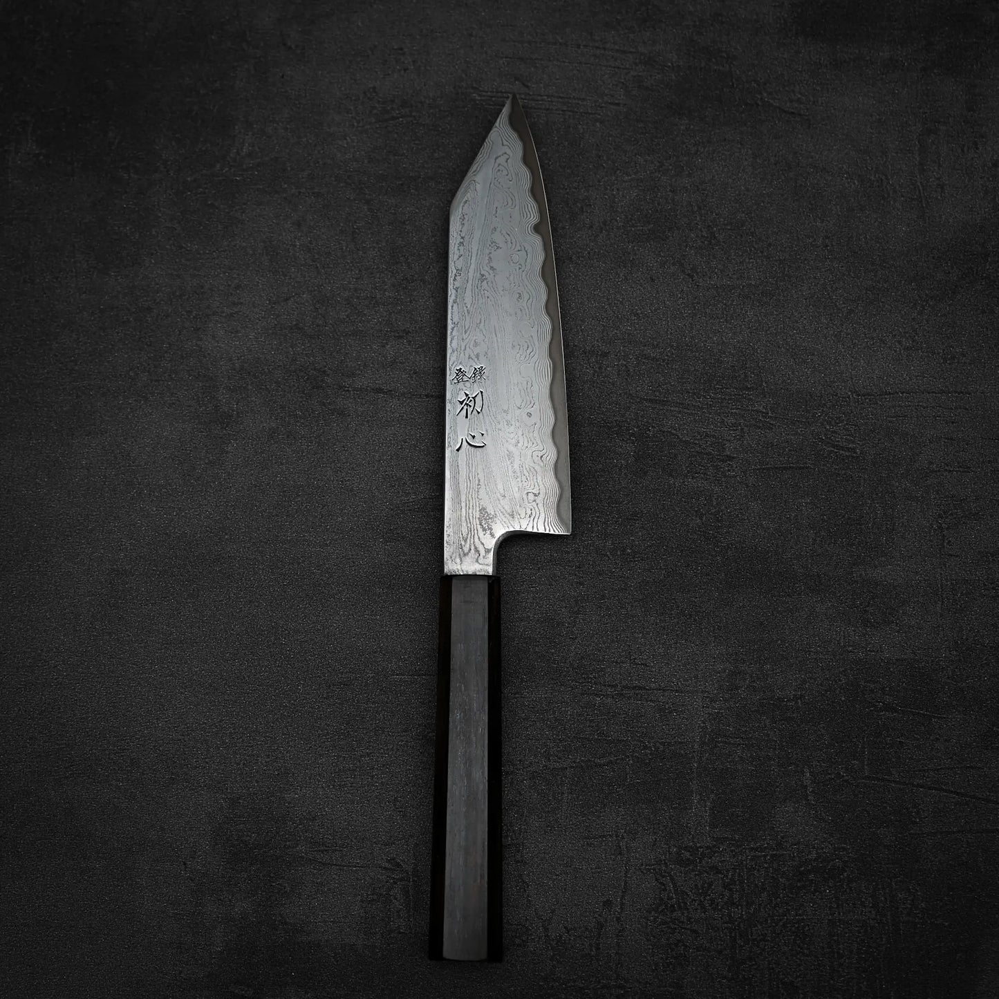 The Satoshi Nakagawa Nakagawa aogami#1 damascus bunka 180mm - etched features a patterned, etched blade with Japanese characters and a dark wooden handle, displayed on a textured surface.
