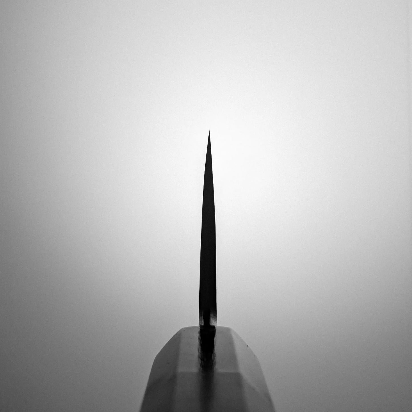 Close-up of the sharp tip on a Satoshi Nakagawa aogami#1 honyaki tall gyuto 240mm, centered against a plain gradient background. Lighting creates a silhouette that highlights the Japanese knife’s exceptional thinness and precision.