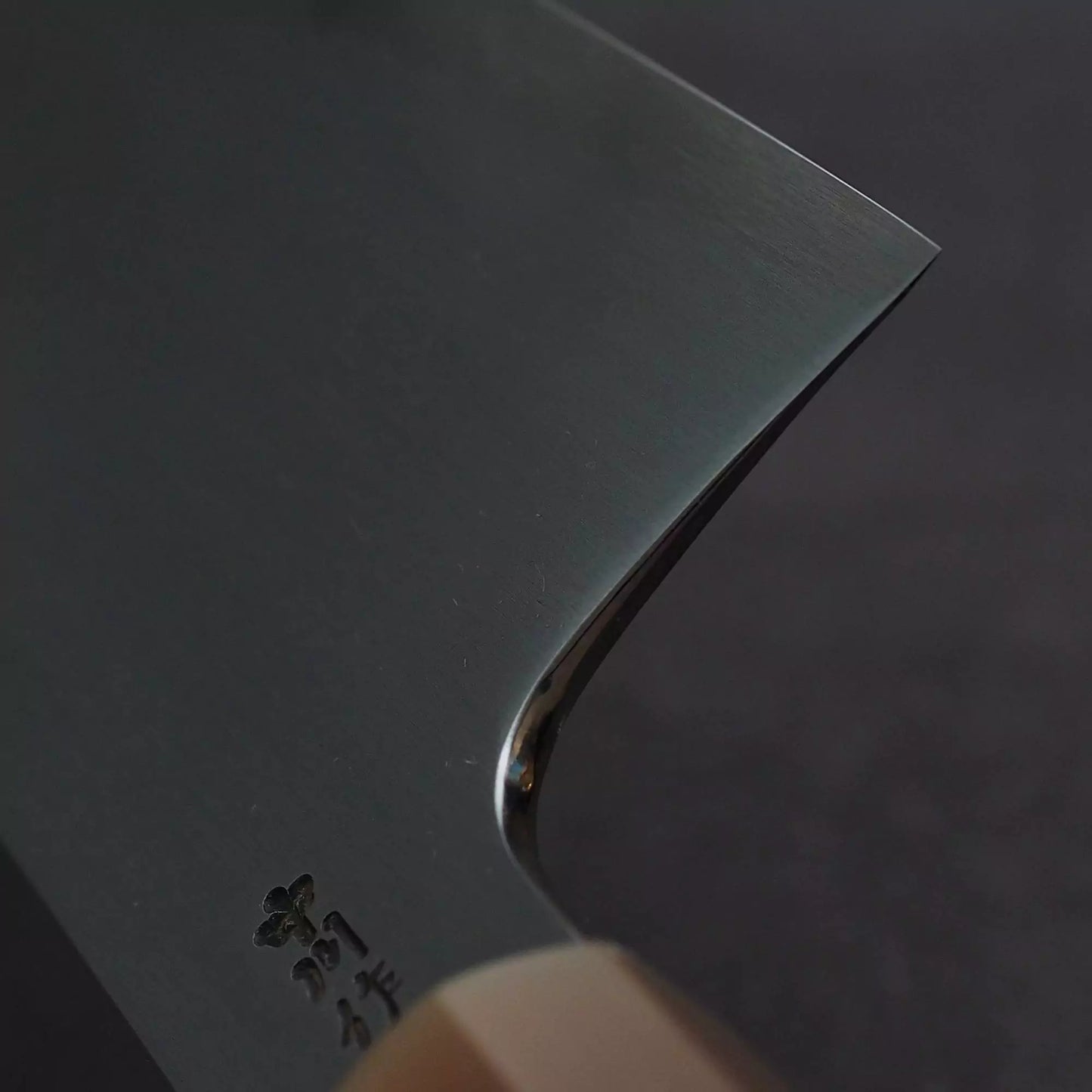 A close-up of the Satoshi Nakagawa bokashi shirogami#1 tall gyuto 240mm shows its wooden handle and detailed Japanese engravings near the base, showcasing premium shirogami#1 steel and masterful craftsmanship against a dark background.