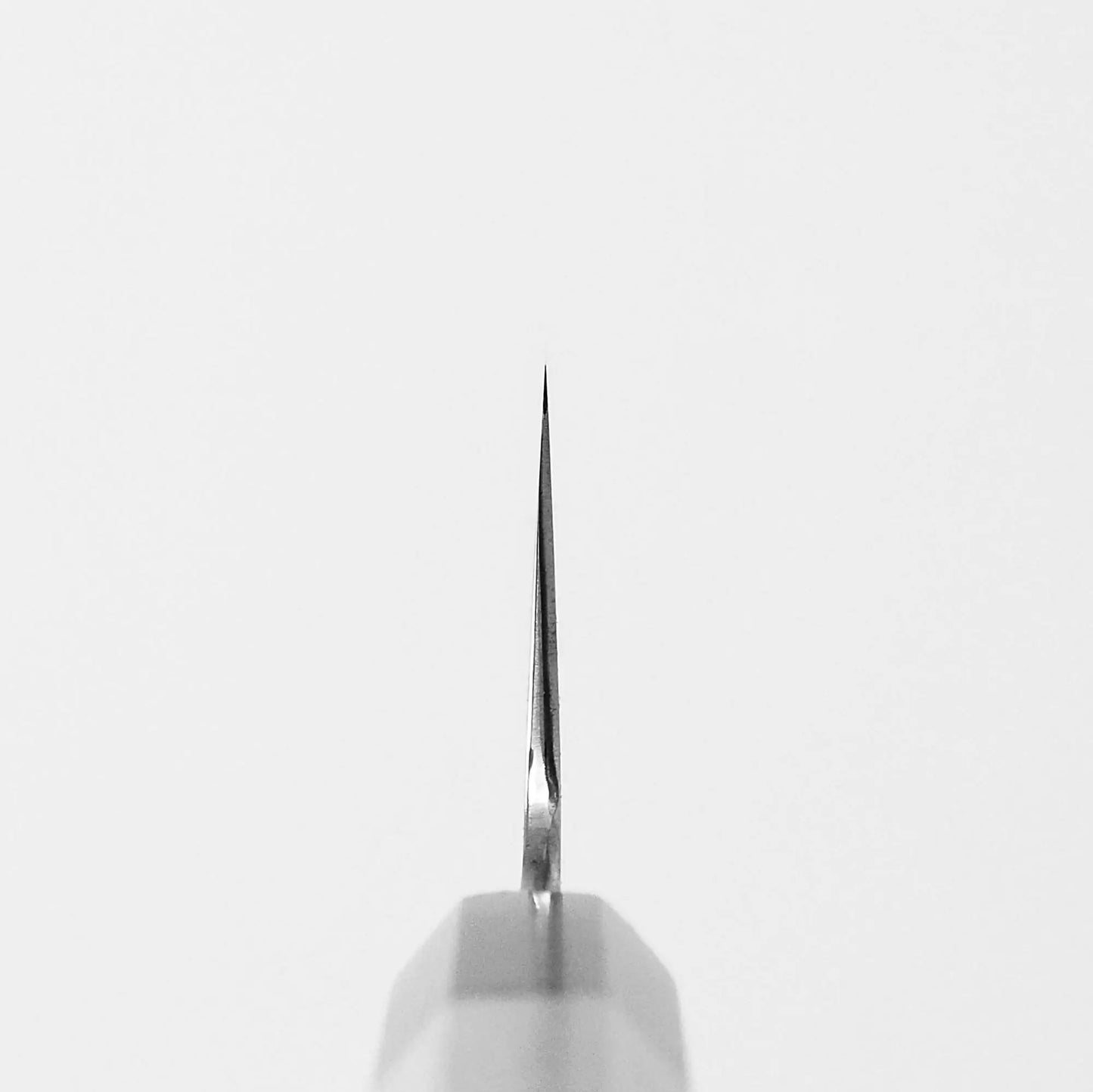 Close-up of the tip of a Satoshi Nakagawa bokashi shirogami#1 tall gyuto 240mm, photographed vertically against a plain white background. The blade is centered, with the tip pointing upward.