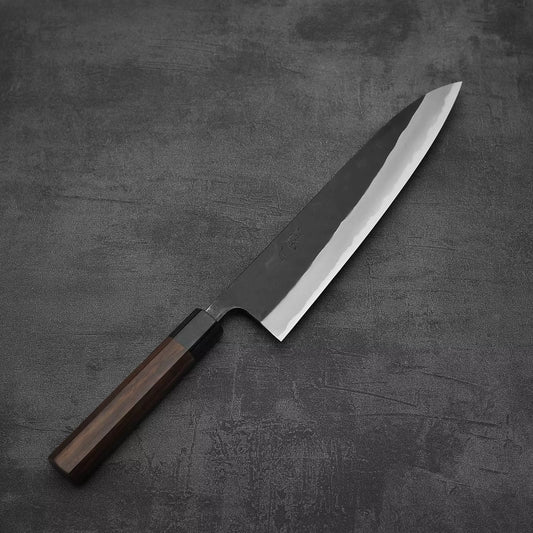 The Nao Yamamoto kurouchi aogami#2 gyuto 240mm, a Japanese chefs knife with a rosewood handle and polished aogami#2 steel blade, rests on a dark textured surface.