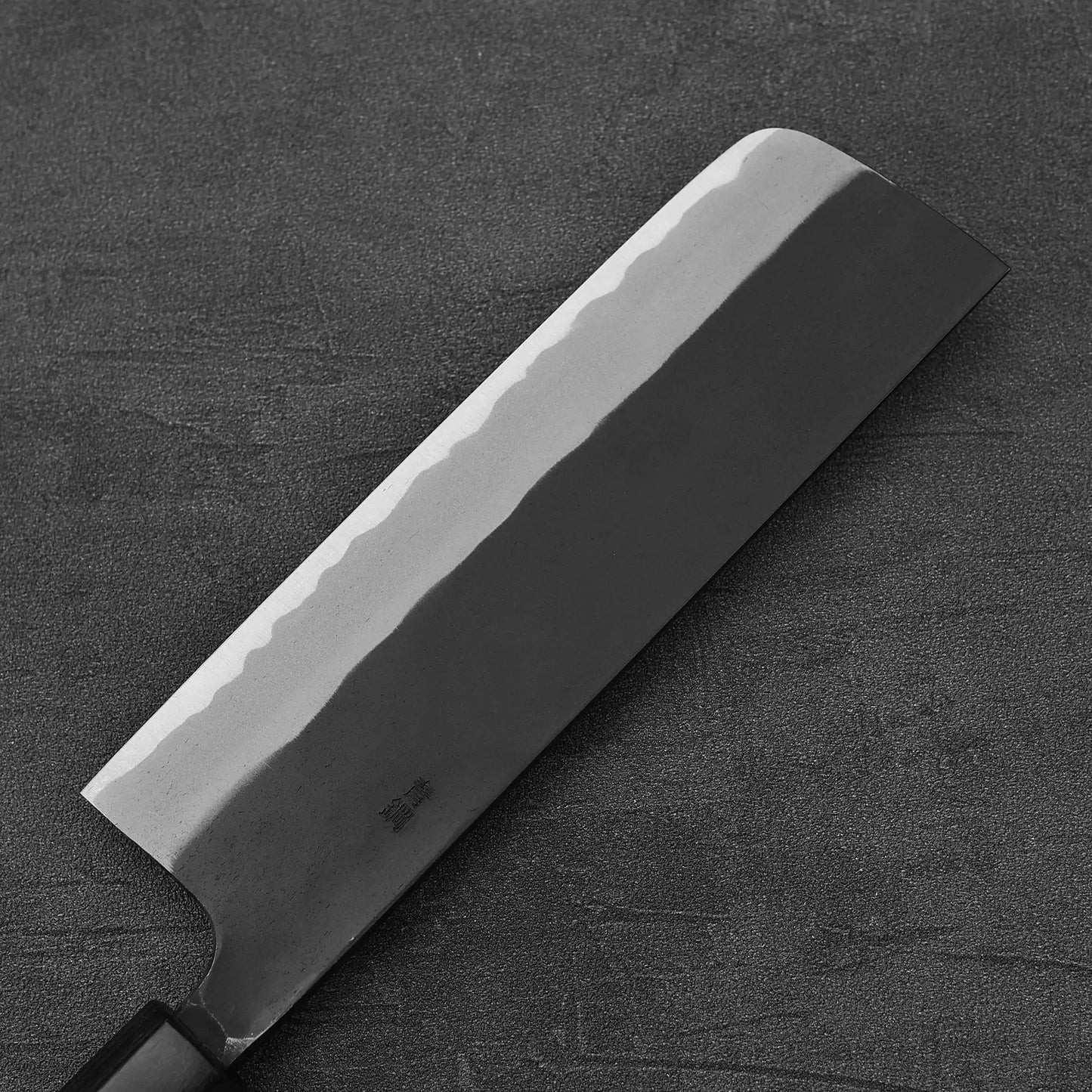 The Nao Yamamoto kurouchi aogami#2 nakiri 180mm features a rectangular blade with a wavy pattern, known for excellent edge retention, resting on a dark textured surface.