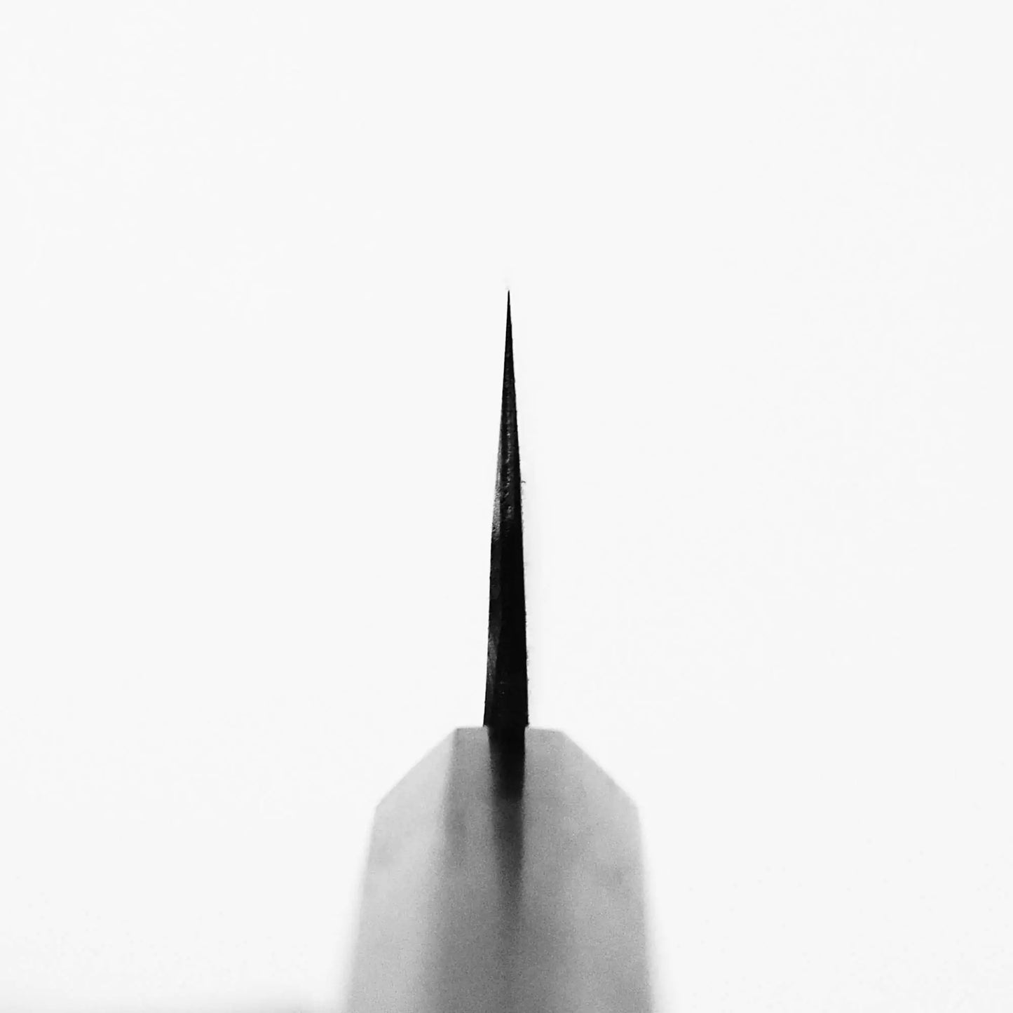Close-up of the tip of a sharp Nao Yamamoto kurouchi shirogami#2 gyuto 210mm blade, photographed from above and centered on a plain white background.