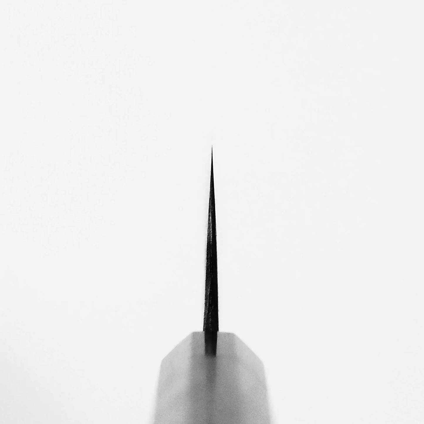 Close-up of the pointed tip of the Nao Yamamoto kurouchi shirogami#2 gyuto 240mm, centered on a plain white background. The sharp, thin point—crafted from shirogami#2 steel—is highlighted, with the blades sides visible at the bottom.