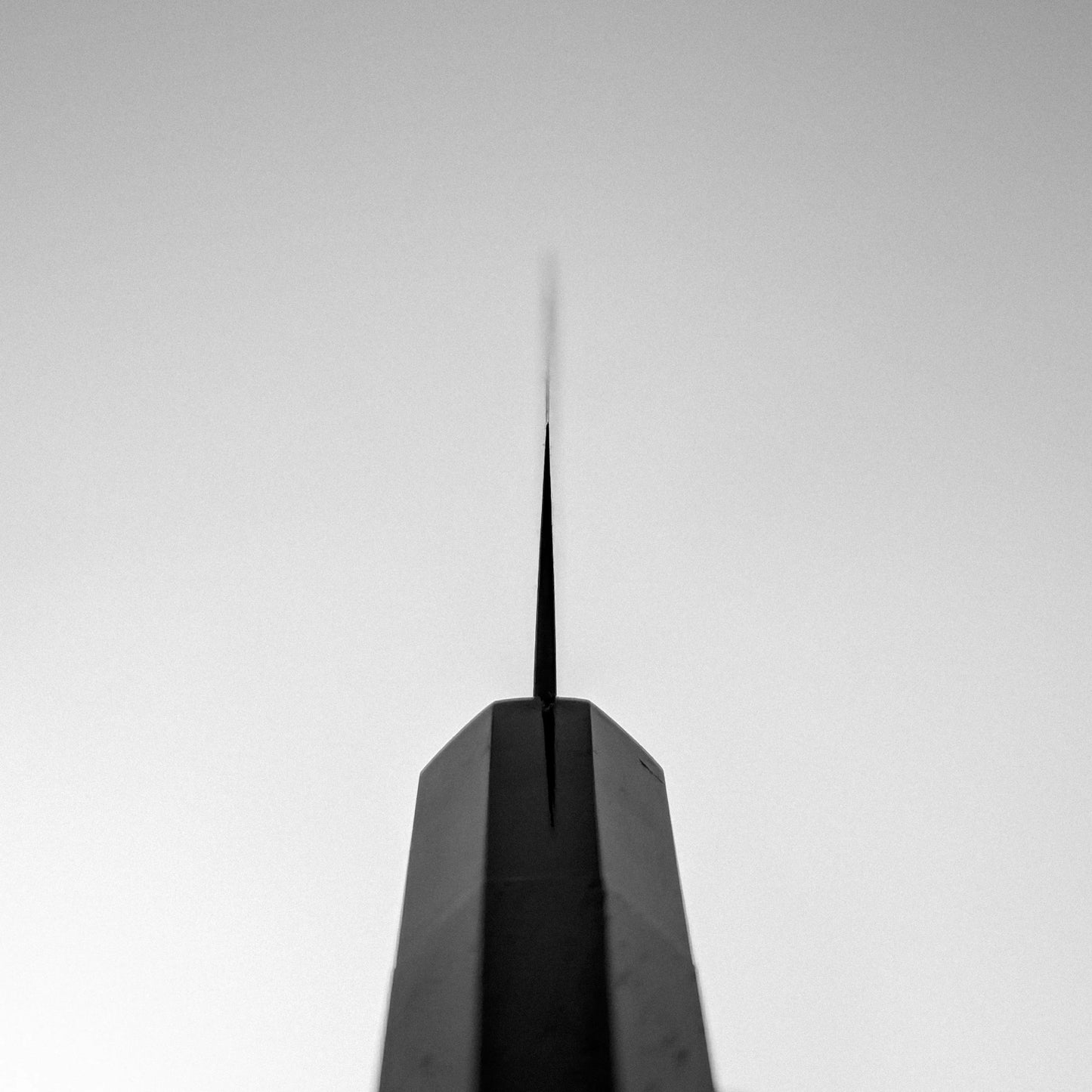 A black and white photo captures the tip of a tall, narrow structure—evoking the precision of the Nigara Hamono Nigara Anmon SG2 damascus petty knife 150mm—against a clear sky, viewed from below with its point centered.