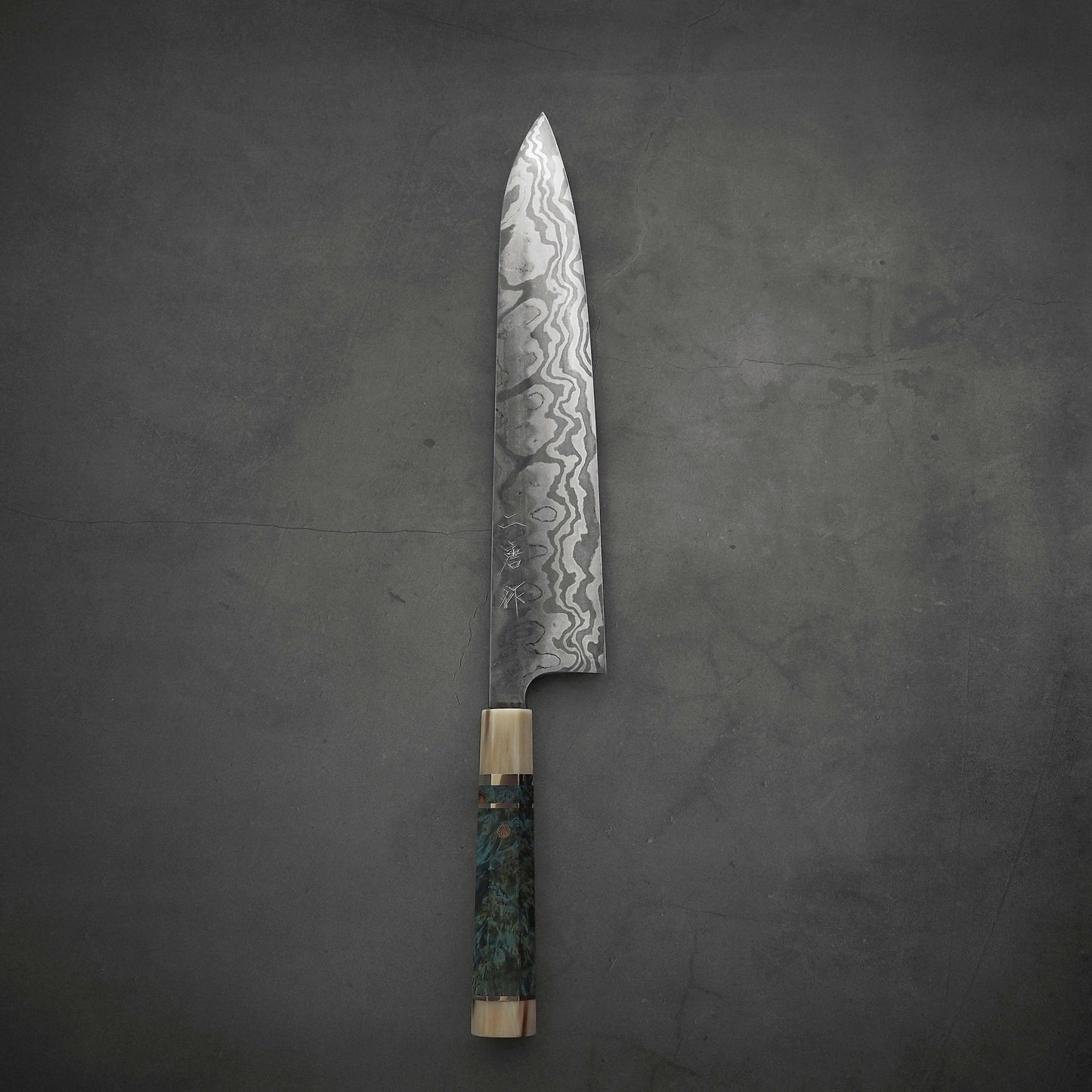 The Nigara Hamono Nigara aogami#2 + shirogami#2 coreless honyaki gyuto 300mm, with its patterned wavy steel blade and wooden handle, rests flat on a dark textured surface.