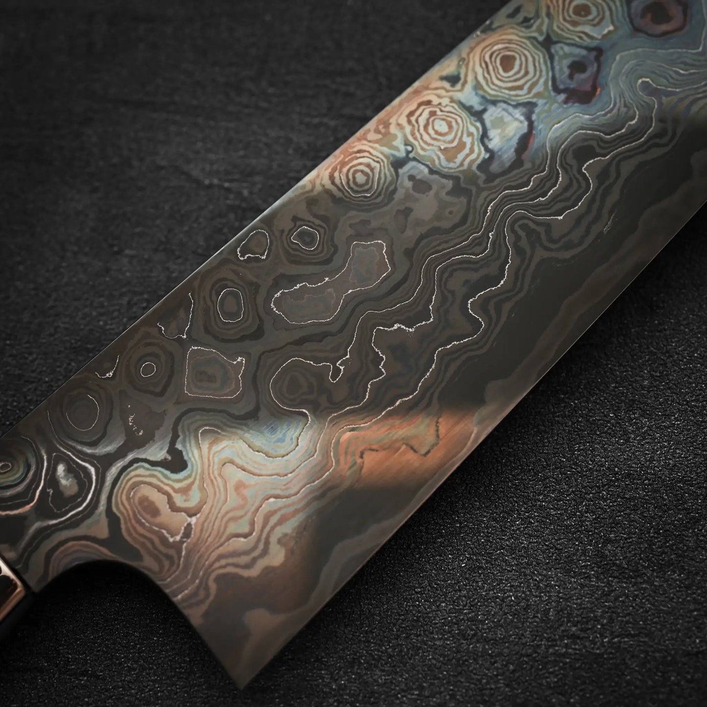 A close-up of the Nigara Hamono Nigara aogami#2 + shirogami#2 coreless damascus gyuto 240mm blade, highlighting its intricate wavy Damascus patterns against a dark, textured background.