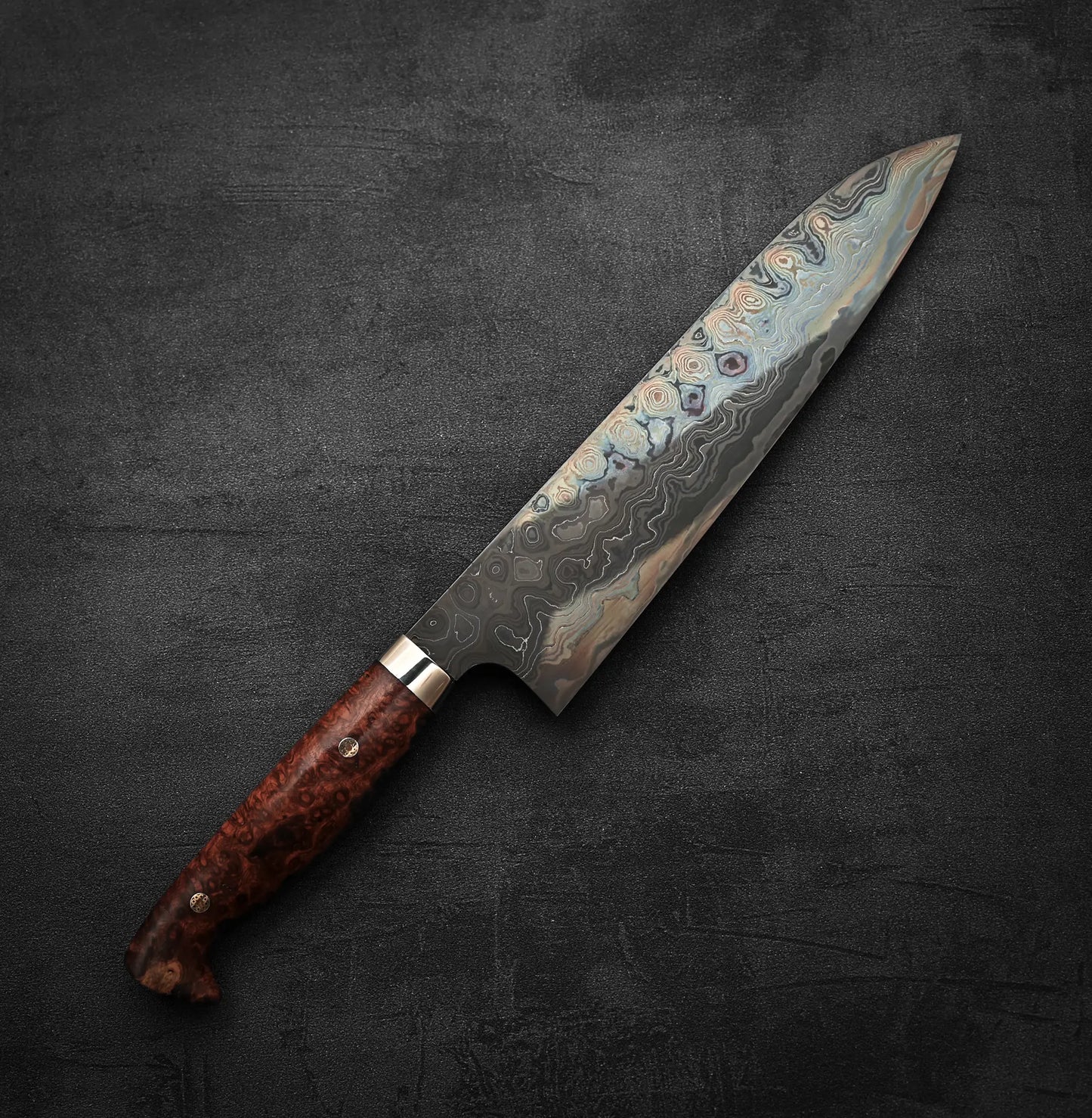 A Nigara Hamono aogami#2 + shirogami#2 coreless damascus gyuto 240mm with a wavy-patterned blade and brown wooden handle, displayed on a dark textured surface.