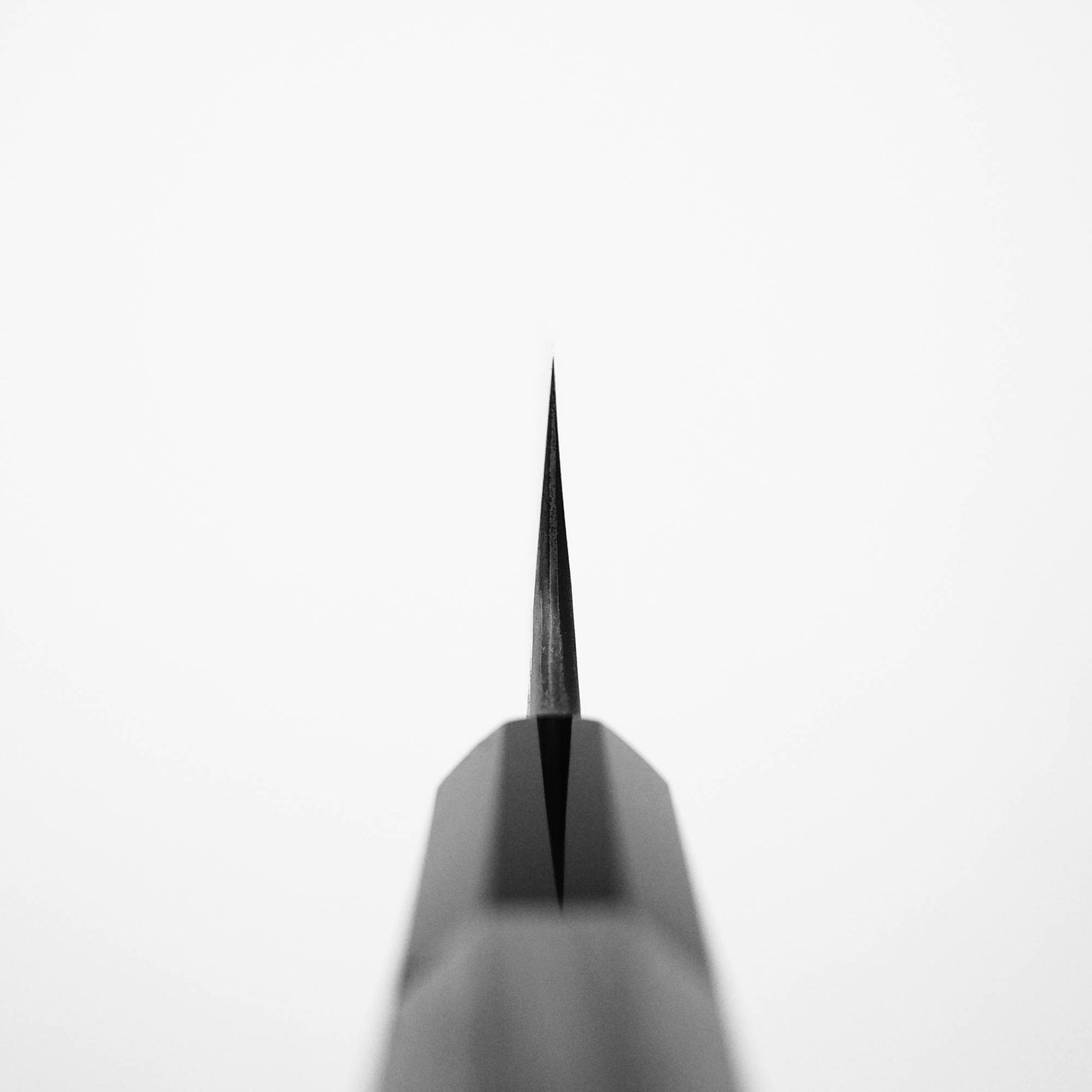 Close-up, black and white photo of the sharp tip of a pencil, echoing the precise edge of Nigara Hamono’s Nigara Kurozome damascus ginsan gyuto 240mm knife, shot from above on a plain white background.