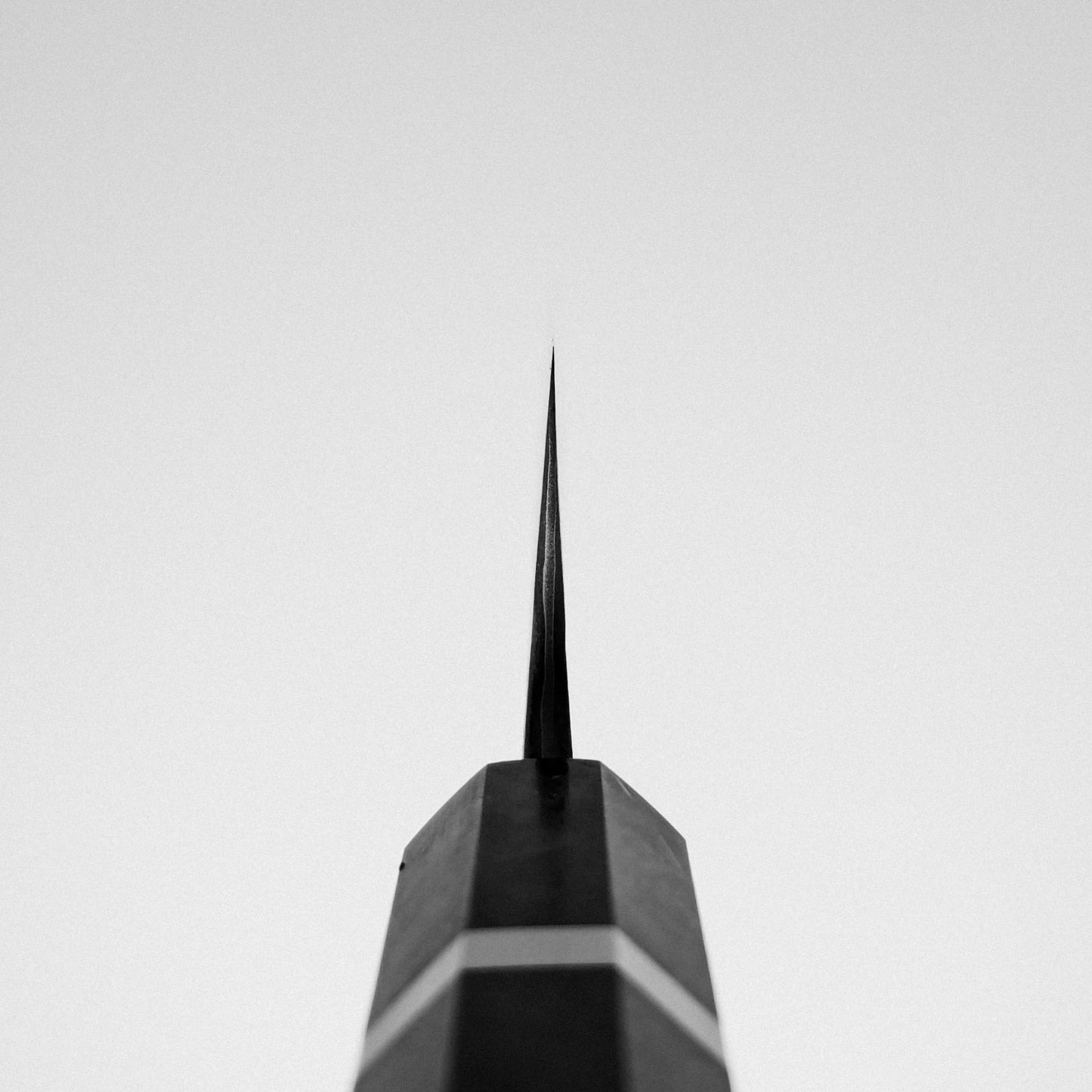 A sharp metal spire rises against a pale gray sky, its black-and-white geometric symmetry echoing the blade of the Nigara Hamono Nigara Kurozome damascus ginsan gyuto 240mm Japanese chefs knife.