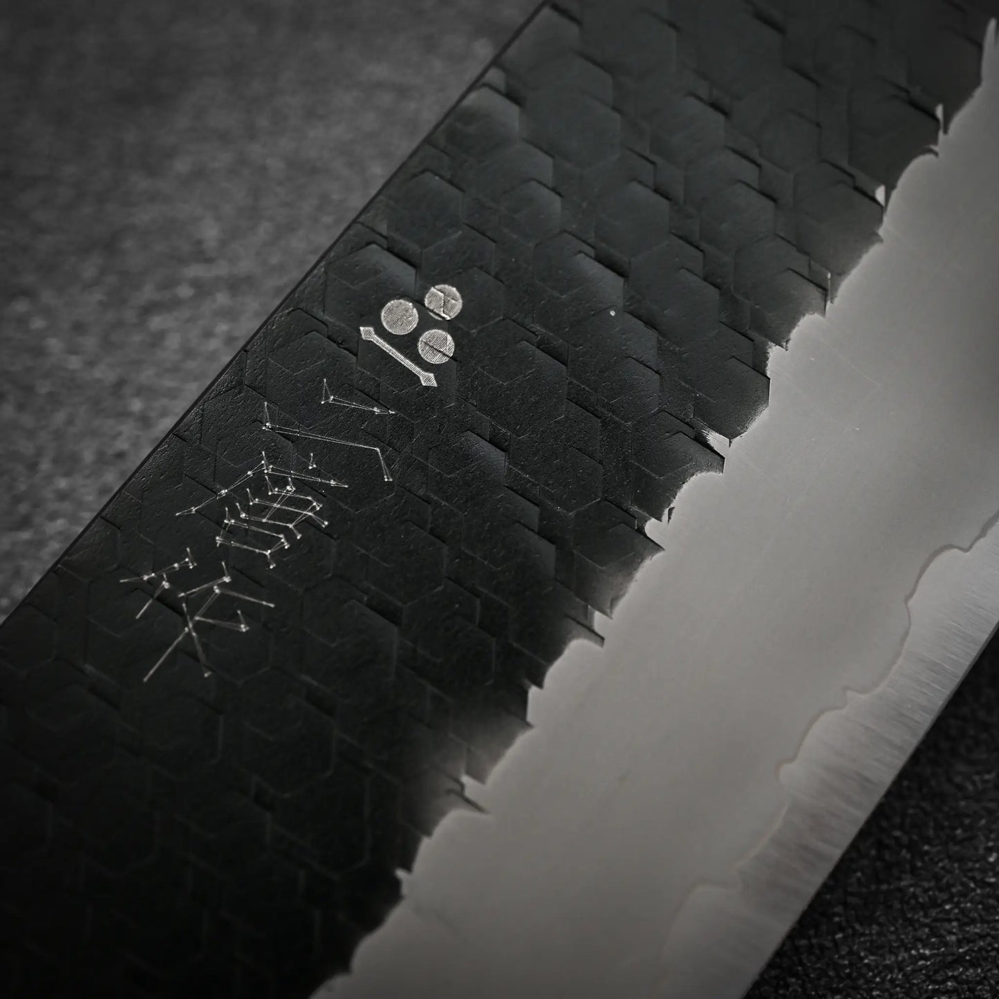 Close-up of a Nigara Hamono Nigara tsuchime kurouchi SG2 kiritsuke gyuto 210mm blade featuring a textured hexagonal pattern, polished silver edge, and engraved characters near the spine.