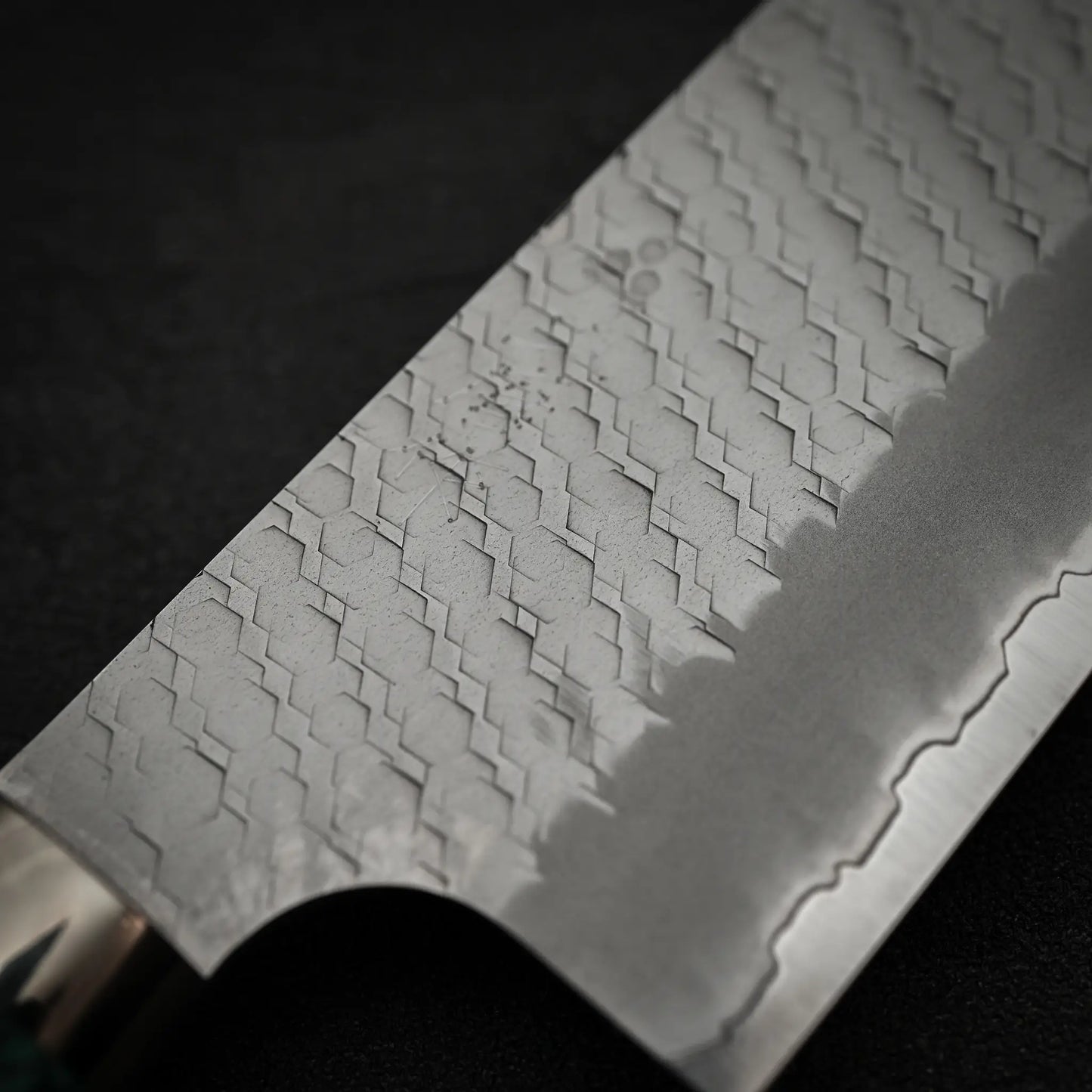 Close-up of the Nigara Hamono Nigara tsuchime SG2 kiritsuke nakiri 180mm, featuring its patterned SG2 stainless steel blade and straight edge, set against a dark background.