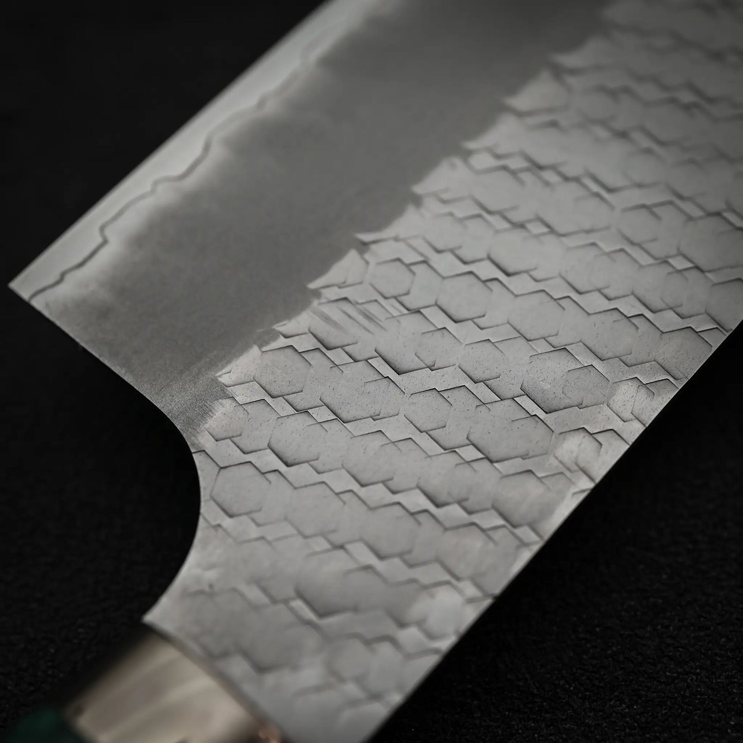 Close-up of the Nigara Hamono Nigara tsuchime SG2 kiritsuke nakiri 180mm blade, showcasing intricate hexagonal Damascus-style patterns in SG2 steel—ideal for precise vegetable prep. A dark, blurred background enhances its fine details.