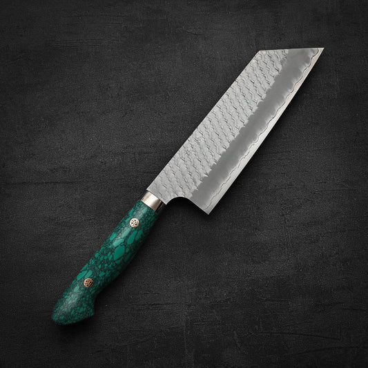 The Nigara Hamono Nigara tsuchime SG2 kiritsuke nakiri 180mm, featuring a patterned SG2 stainless steel blade and a green marbled handle, is displayed on a textured dark surface.