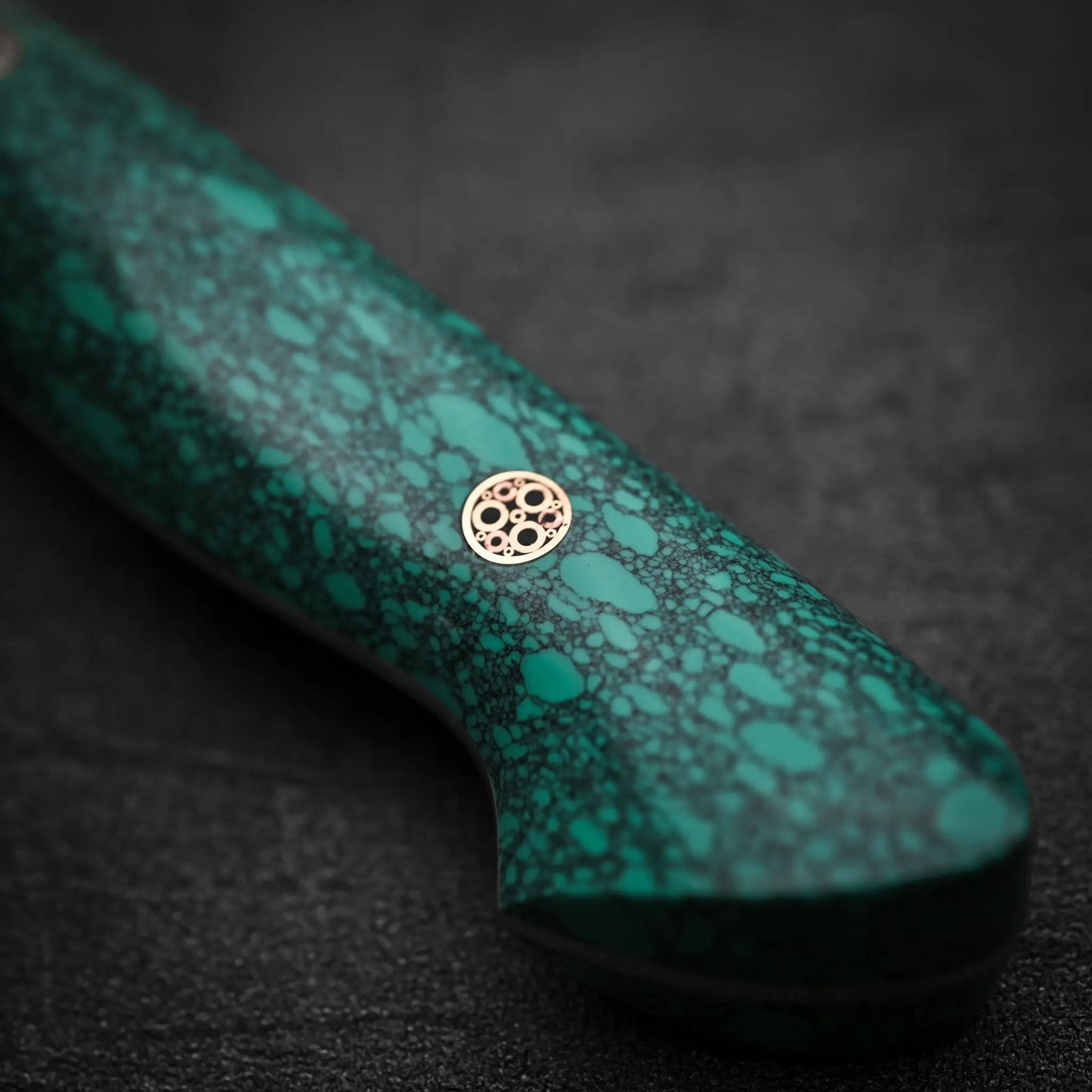 Close-up of the Nigara Hamono Nigara tsuchime SG2 kiritsuke nakiri 180mm handle, featuring a green speckled pattern and a decorative circular metal pin—ideal for precise vegetable prep—set against a dark background.